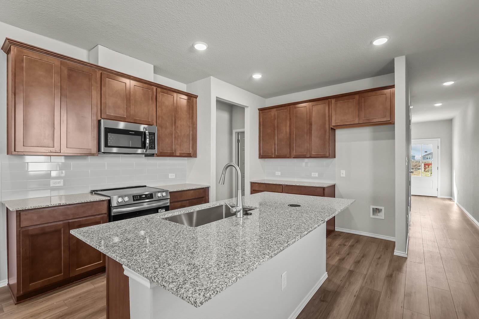 Modern kitchen with granite island, wood cabinets, and stainless appliances in The Frio F plan at Heartland, Texas.