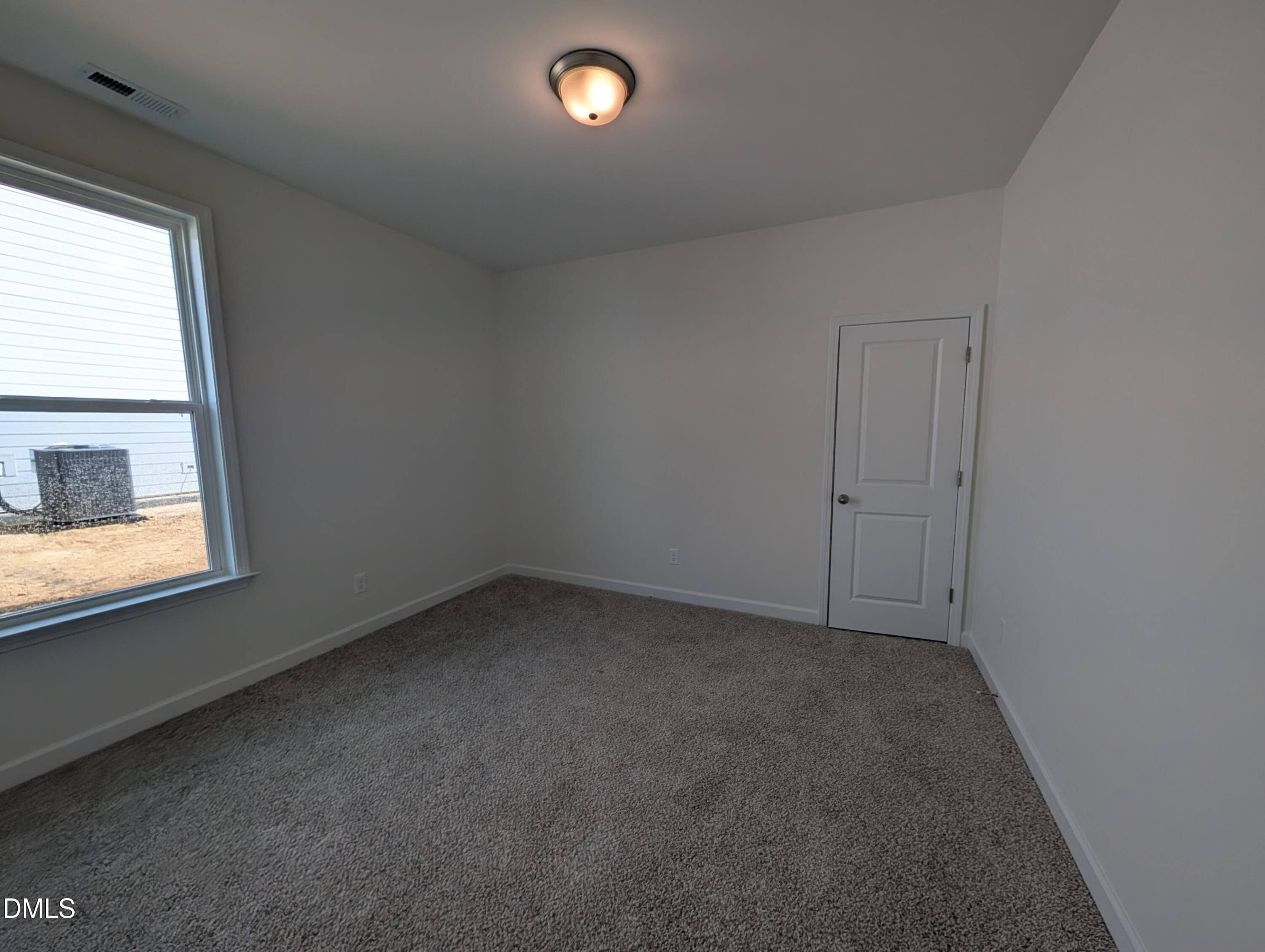 Empty bedroom with gray carpet, white walls, ceiling light, and large window in Davidson Homes Magnolia A plan, Wendell, NC