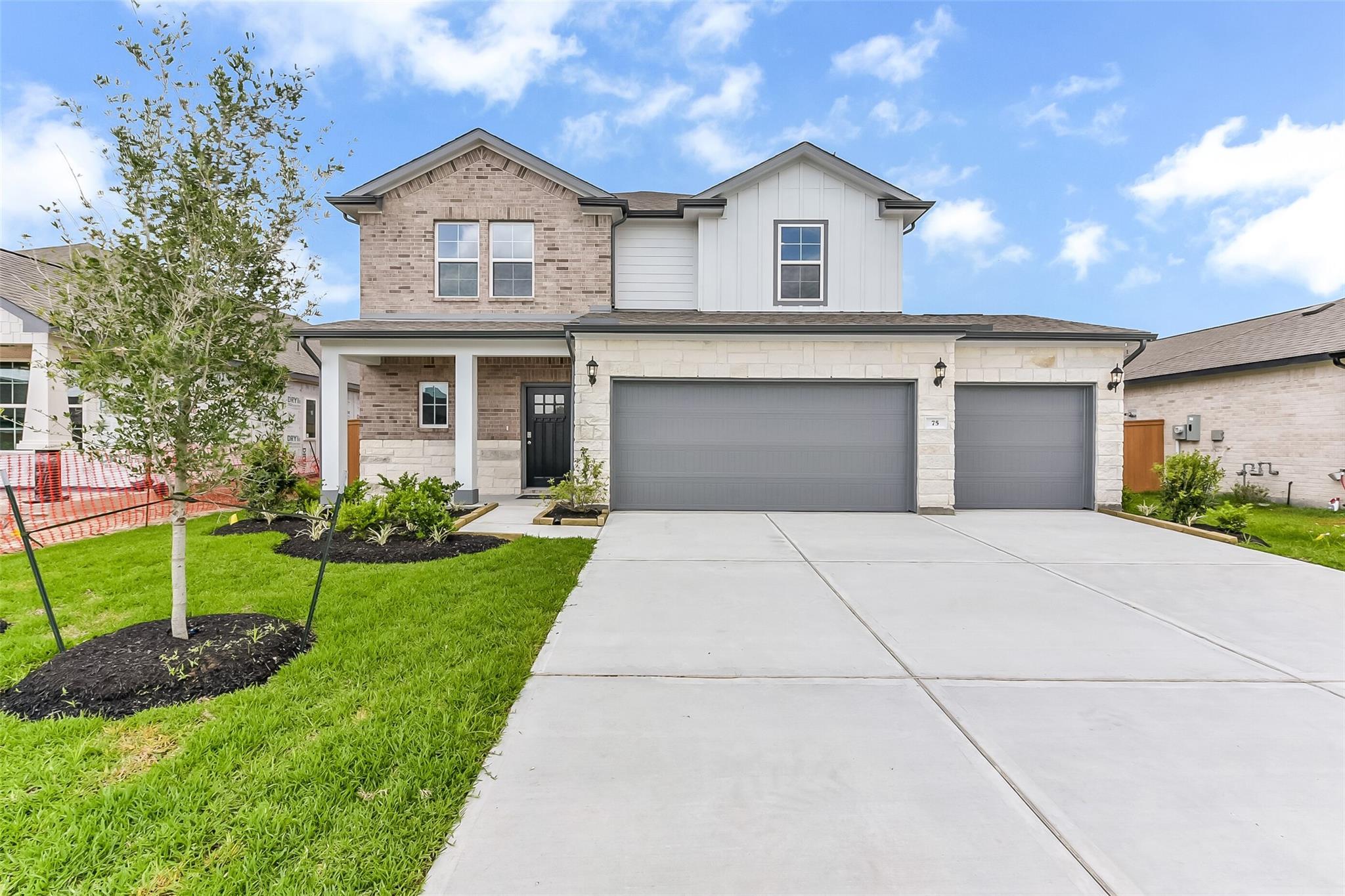 Modern two-story brick and stone home with 3-car garage, covered porch, and landscaped yard in River Ranch Meadows, Dayton, Texas