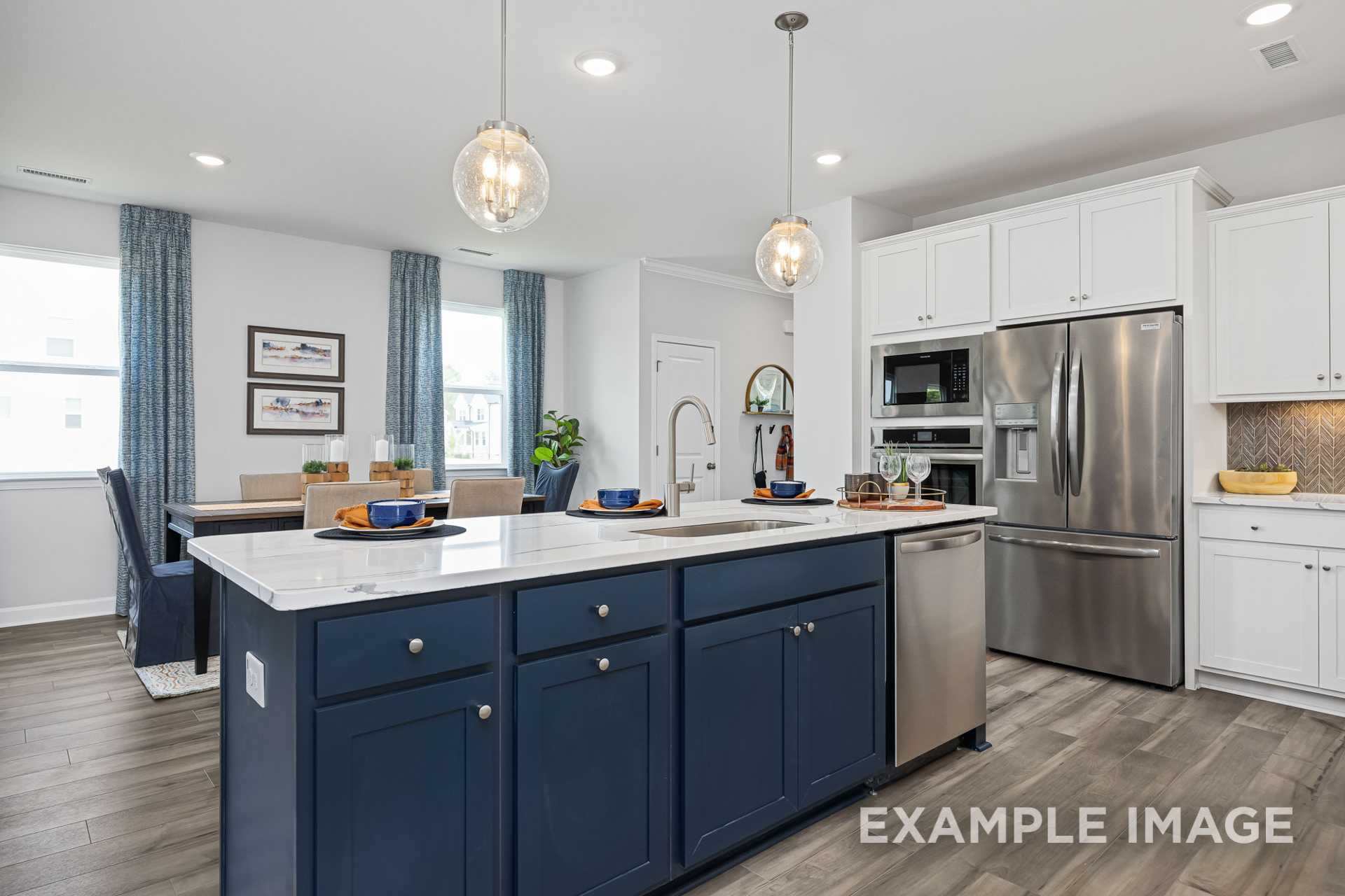 Spacious kitchen in The Adalynn A featuring navy blue island, white cabinets, stainless appliances, and dining nook