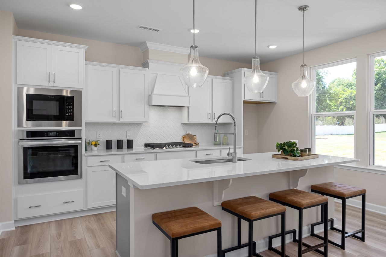 Modern kitchen in The Chestnut A featuring white cabinets, quartz countertops, a large island, and stainless steel appliances.