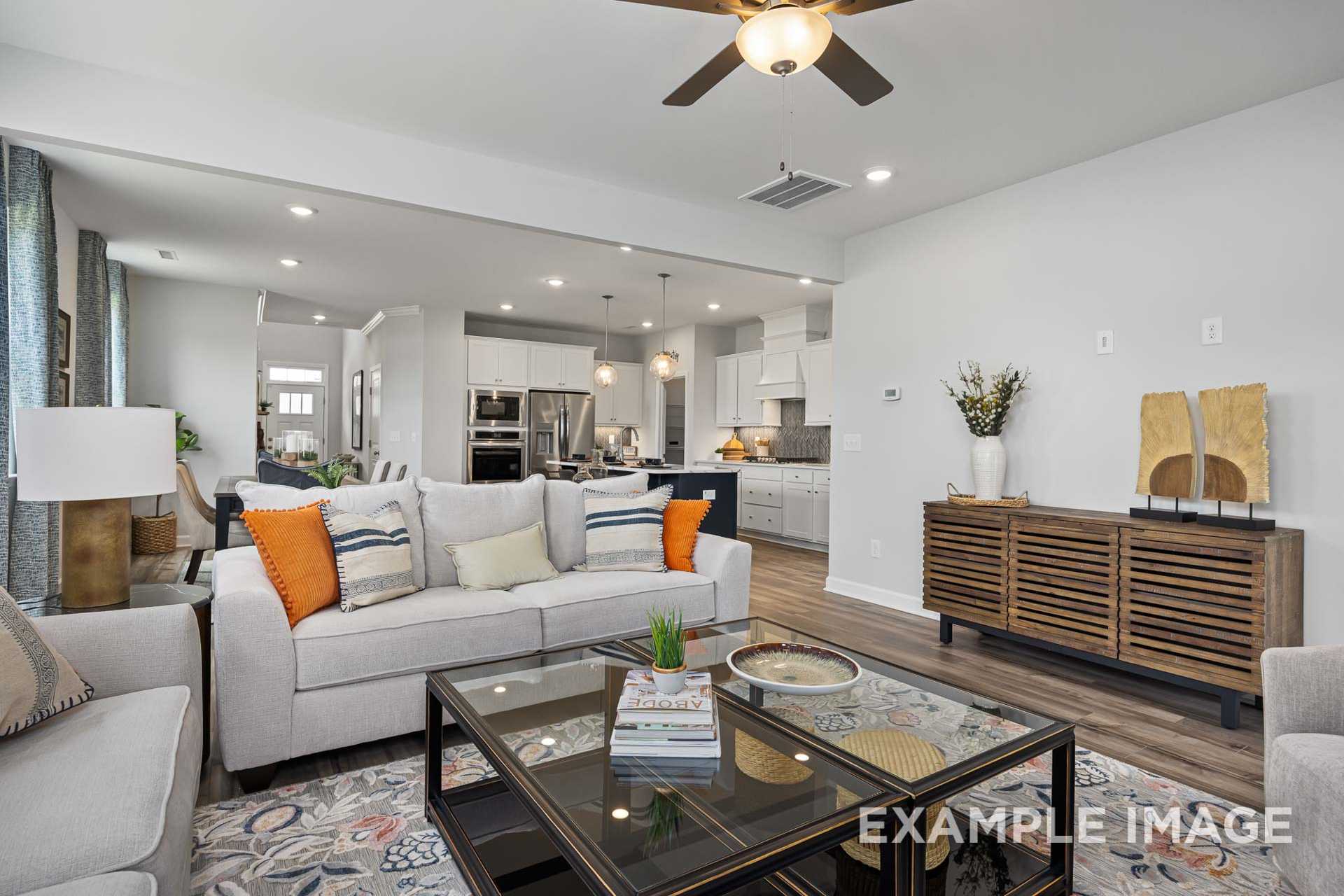 Spacious open-concept living room in The Adalynn A with white sofa, orange accents, modern kitchen island, and ceiling fan