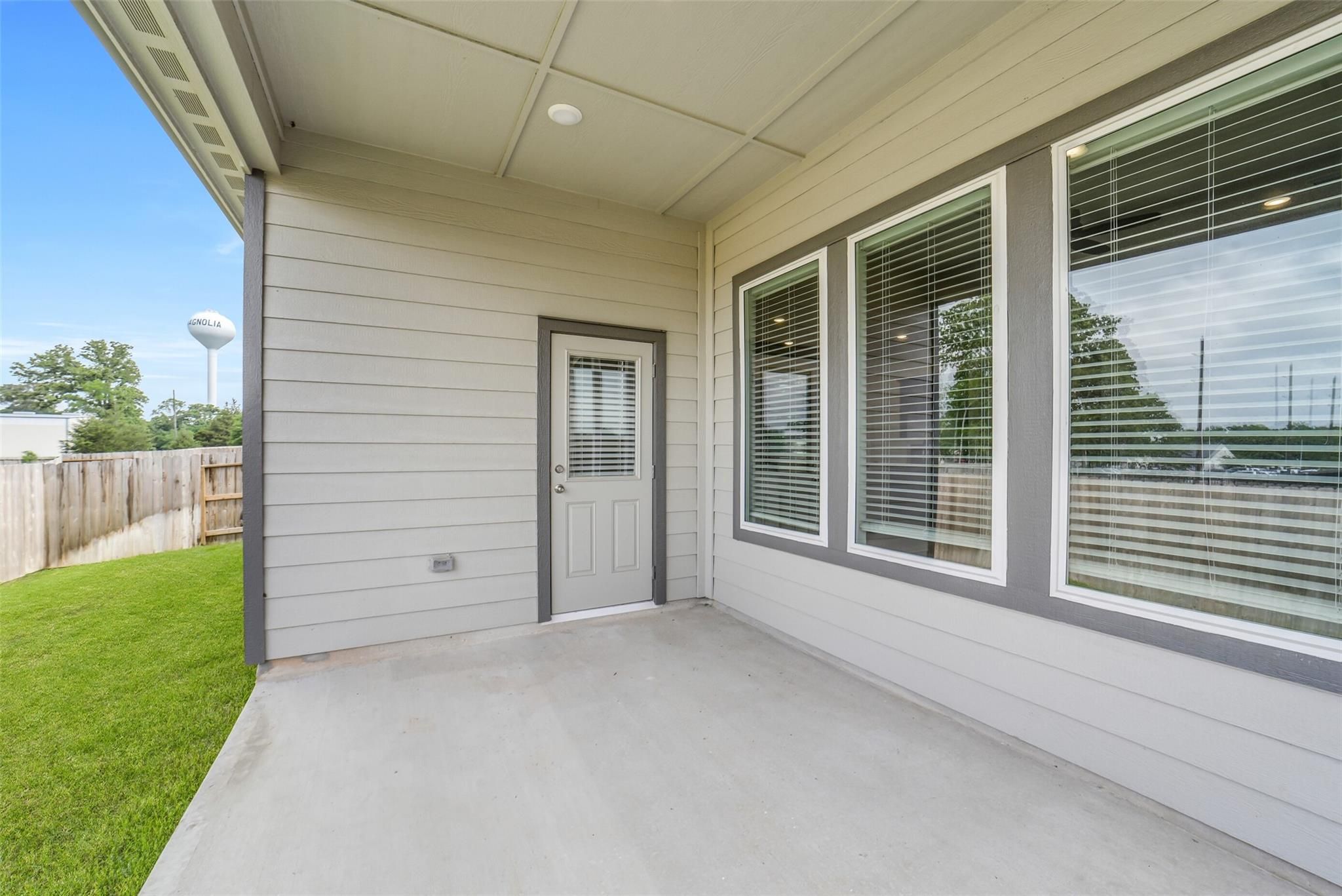 Covered back patio with large shuttered windows, gray French door, and lush green lawn in Davidson Homes The Acadia C, Magnolia TX