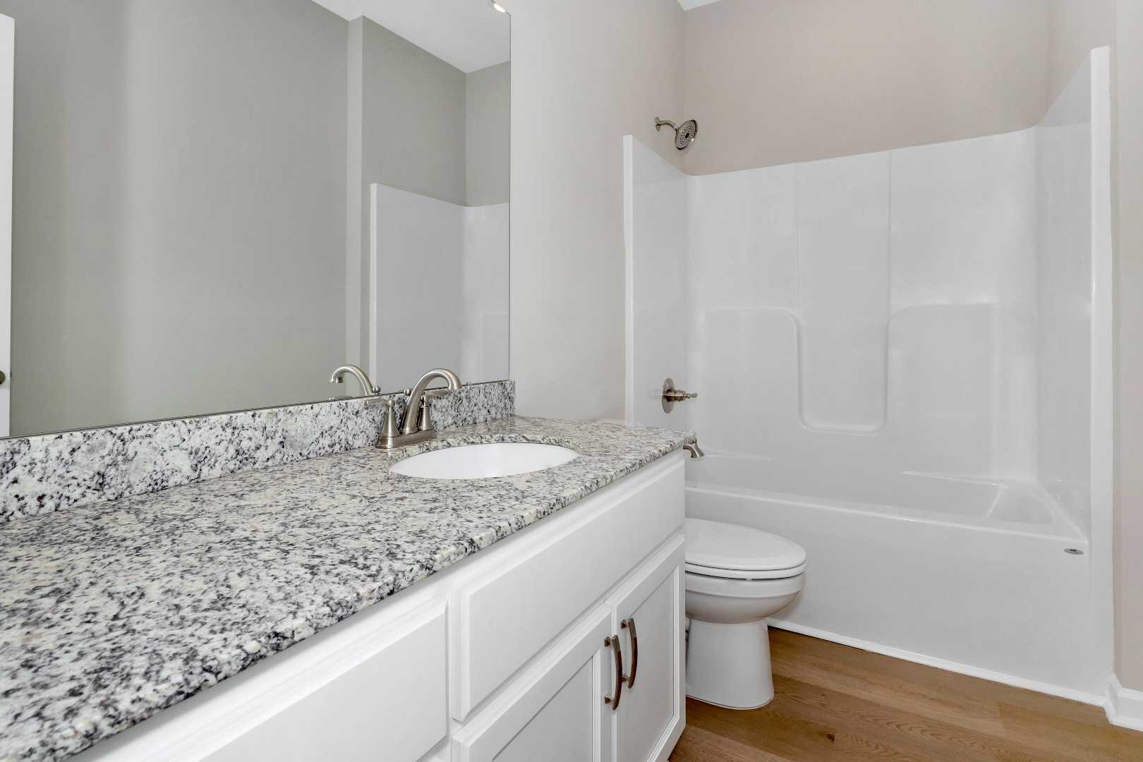 Spacious master bathroom in The Orion featuring white double vanity, granite countertop, tub-shower combo, and hardwood floors