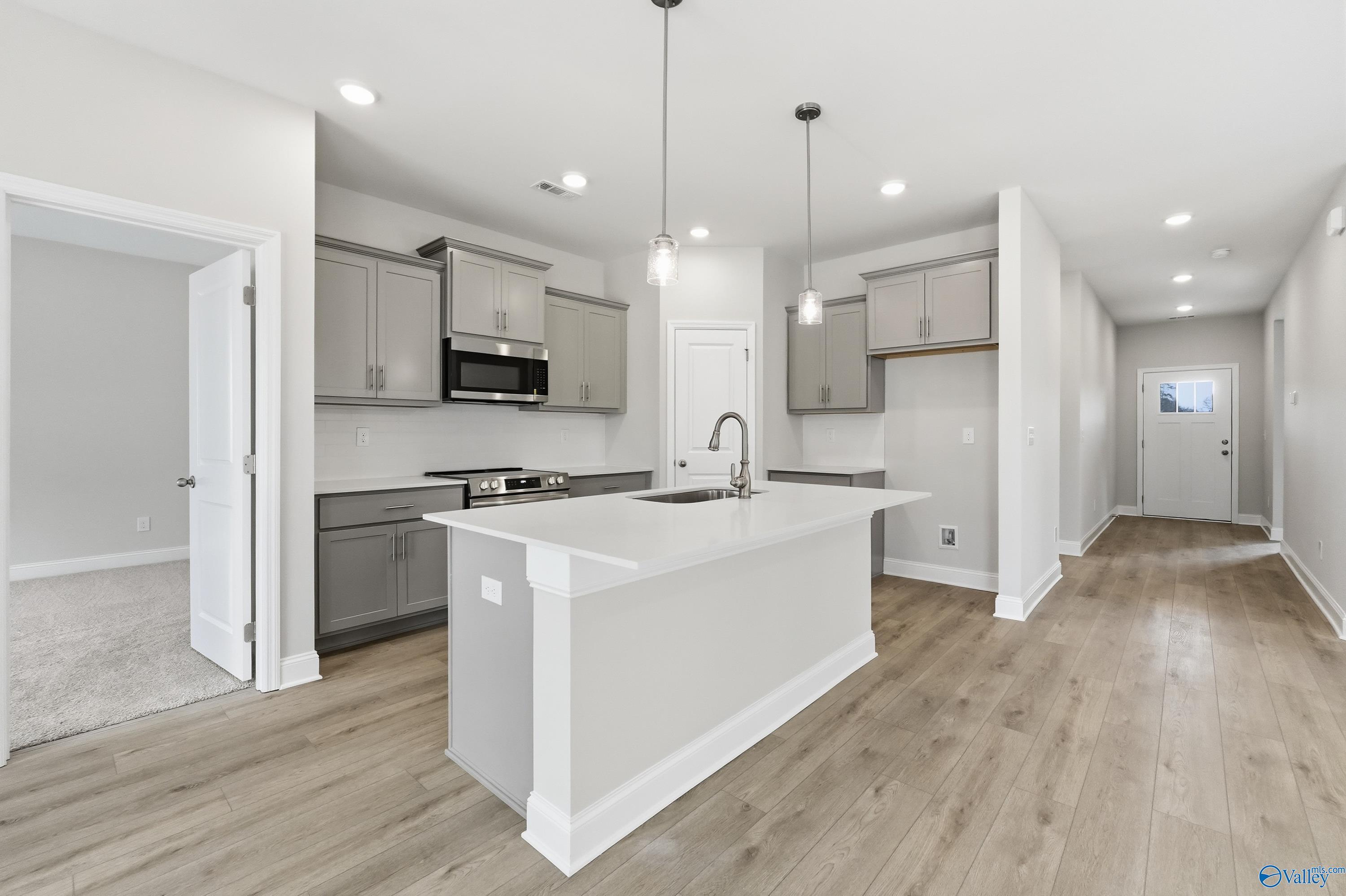 Modern open-concept kitchen with gray cabinets, white quartz island, and pendant lights in The Franklin by Davidson Homes, Meridianville, AL