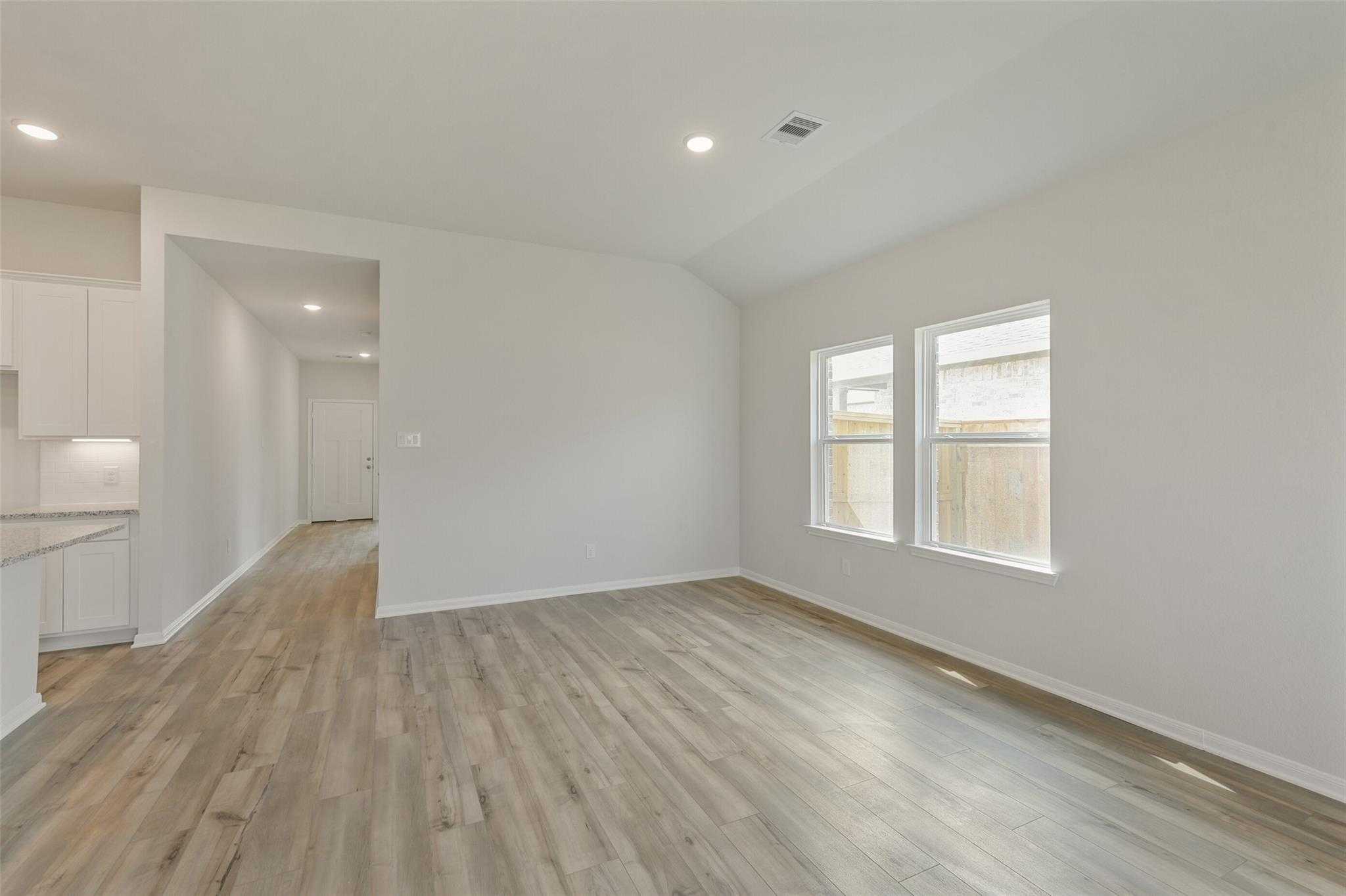 Bright open hallway with wood laminate flooring, white walls, and adjacent kitchen in Davidson Homes The Laguna B, Dayton, TX