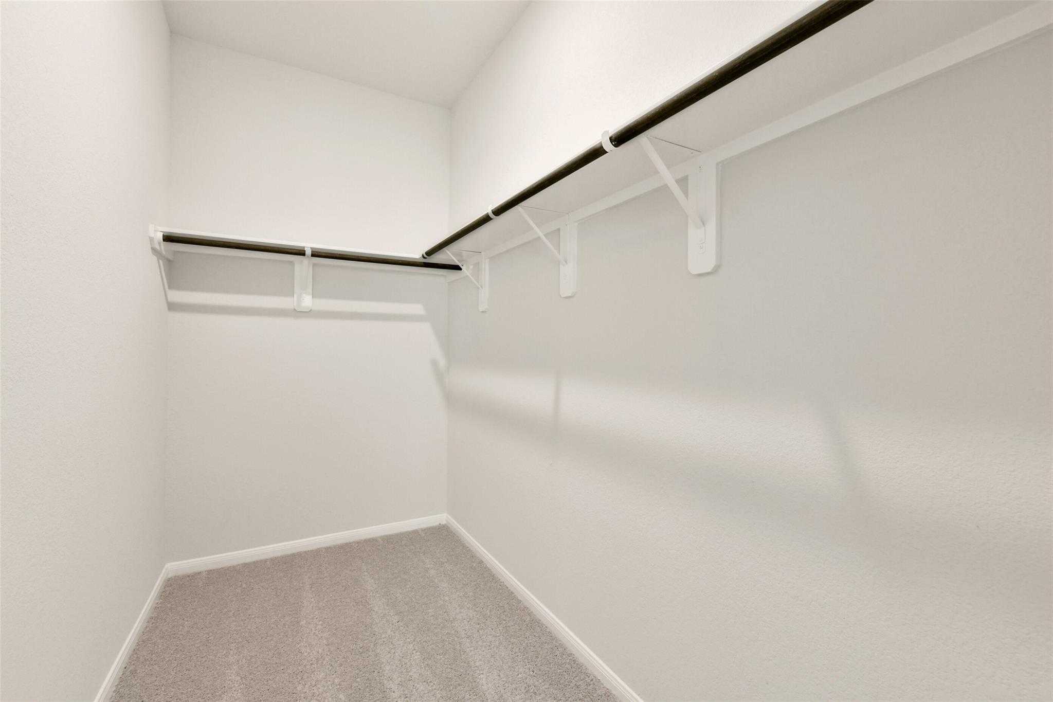 Spacious walk-in closet with white walls, gray carpet floor, and black hanging rods in Davidson Homes The Frio G, Conroe, Texas