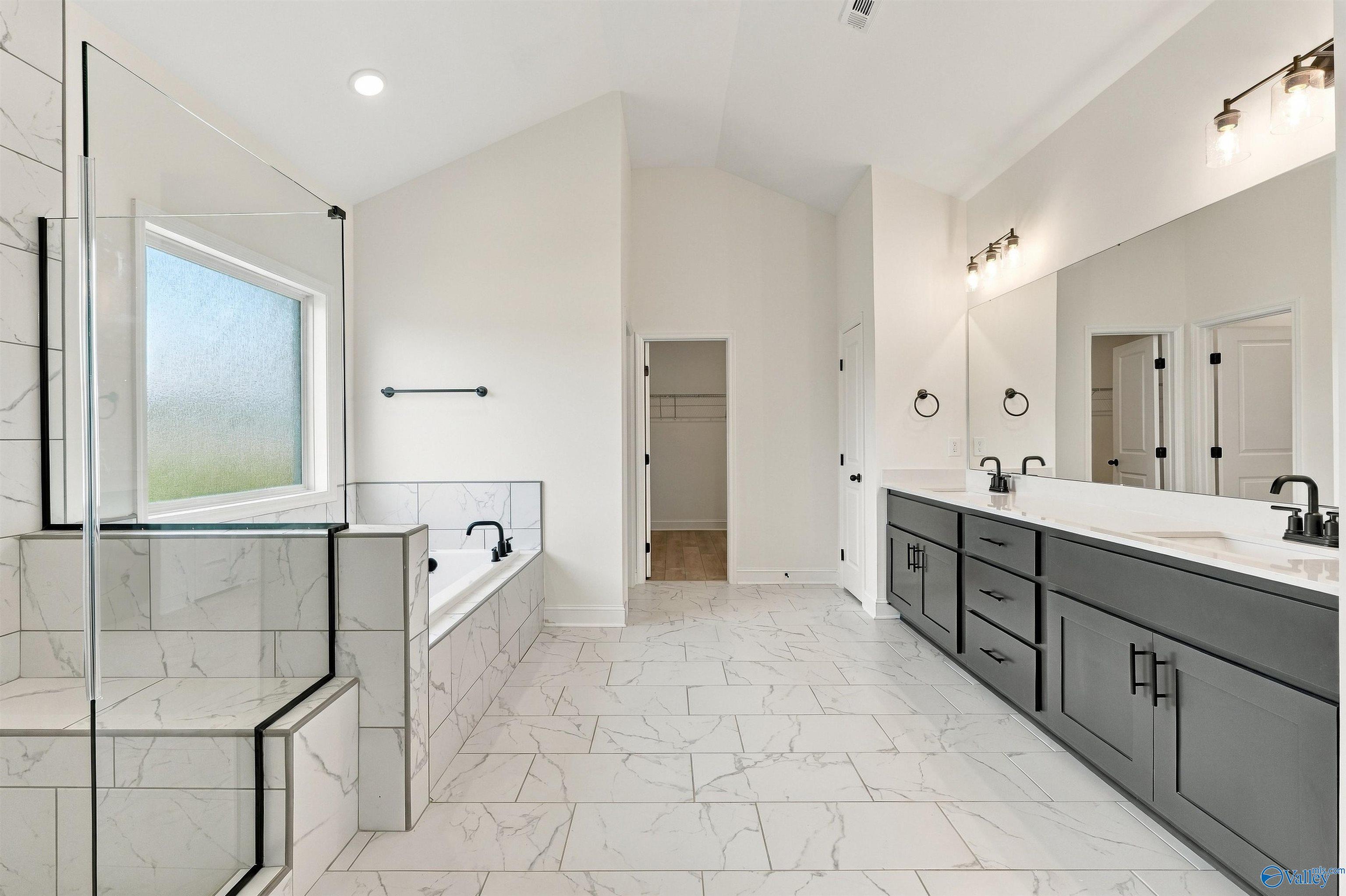 Elegant primary bathroom with marble tile, soaking tub, glass shower, and gray double vanity in Davidson Homes Valencia, Huntsville