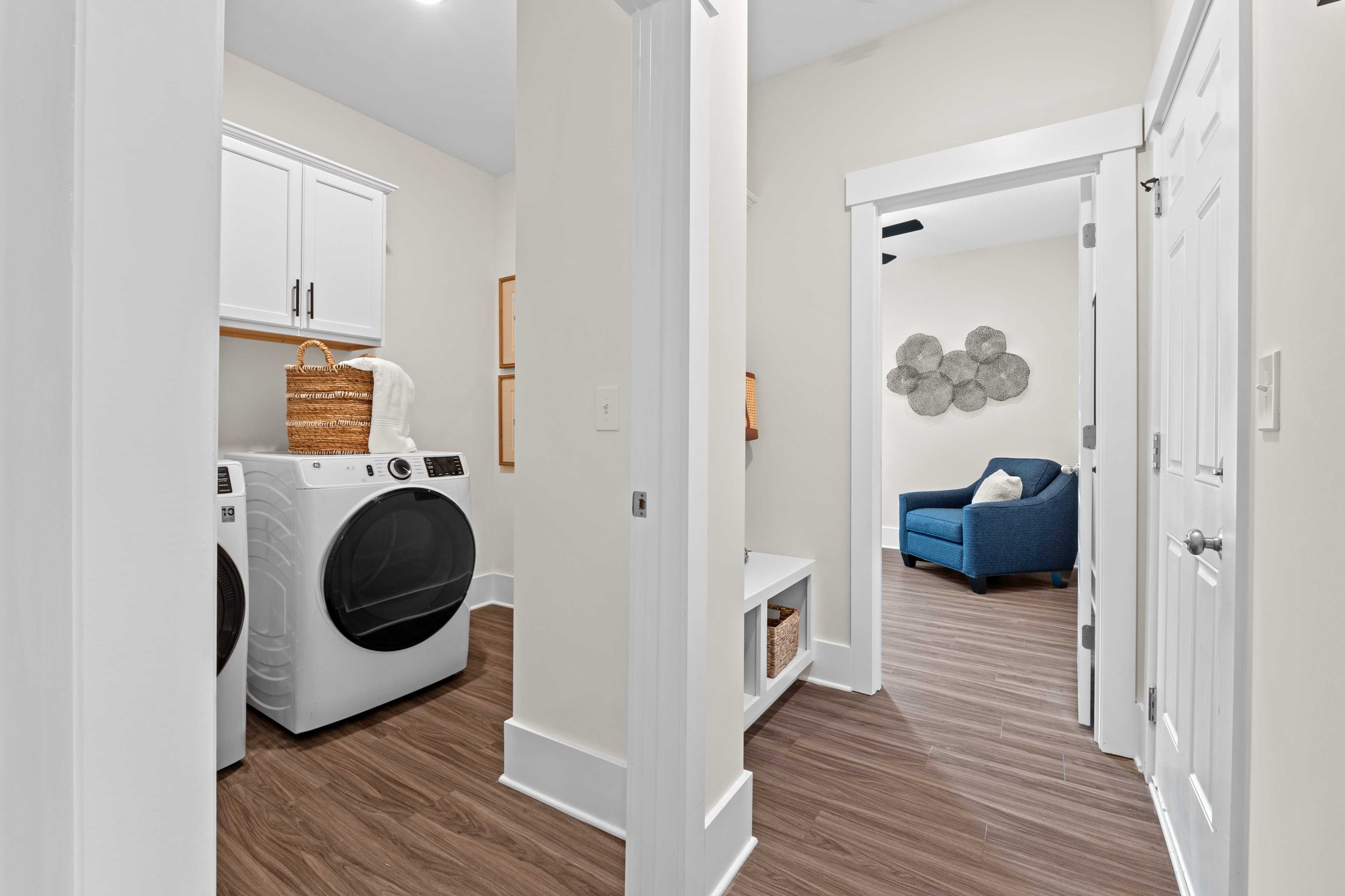 Spacious laundry room and mudroom at Ivy Hills in Toney, Alabama with white cabinets, washer-dryer, hardwood floors, blue accent chair
