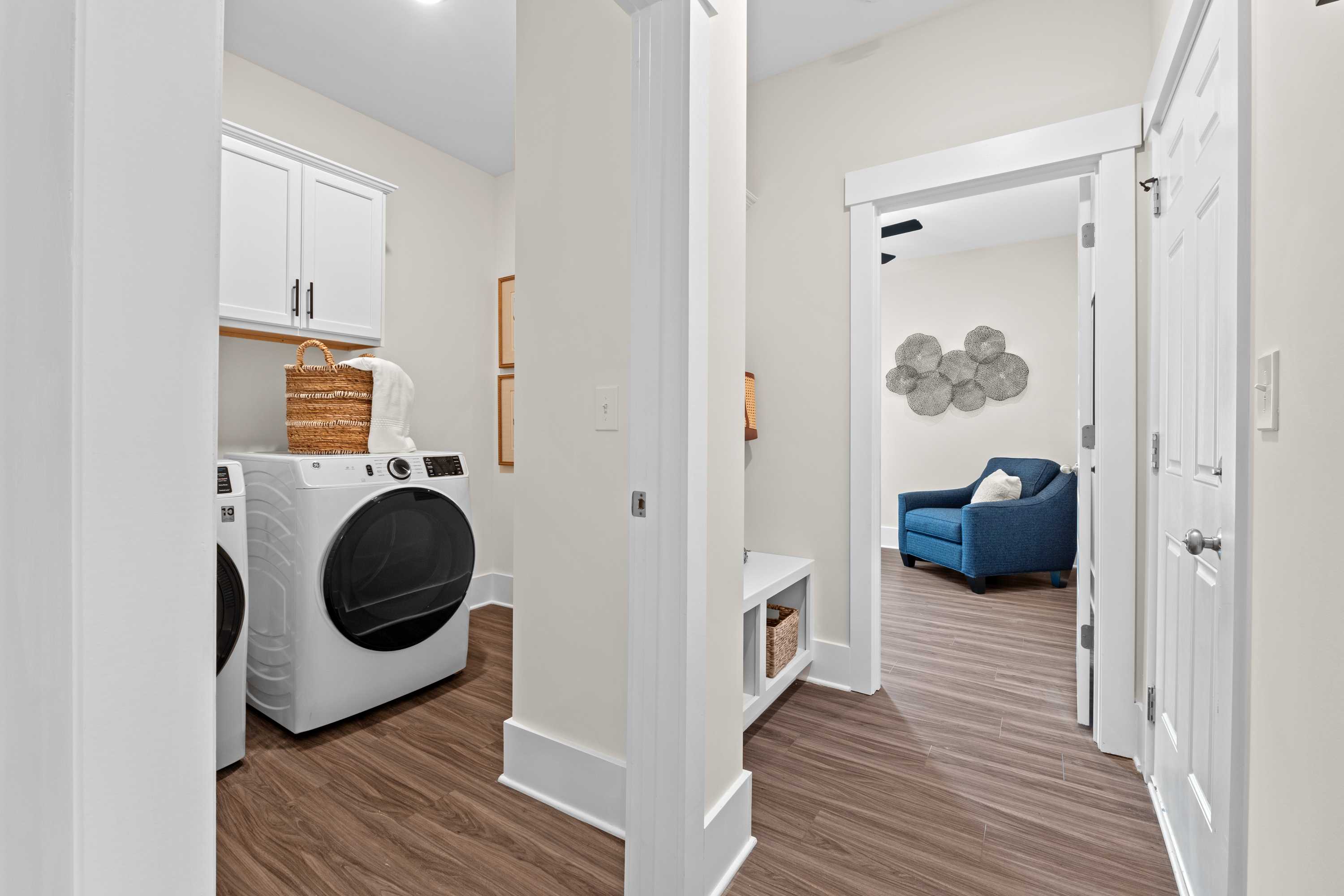 Spacious laundry room and mudroom at Ivy Hills in Toney, Alabama with white cabinets, washer-dryer, hardwood floors, blue accent chair