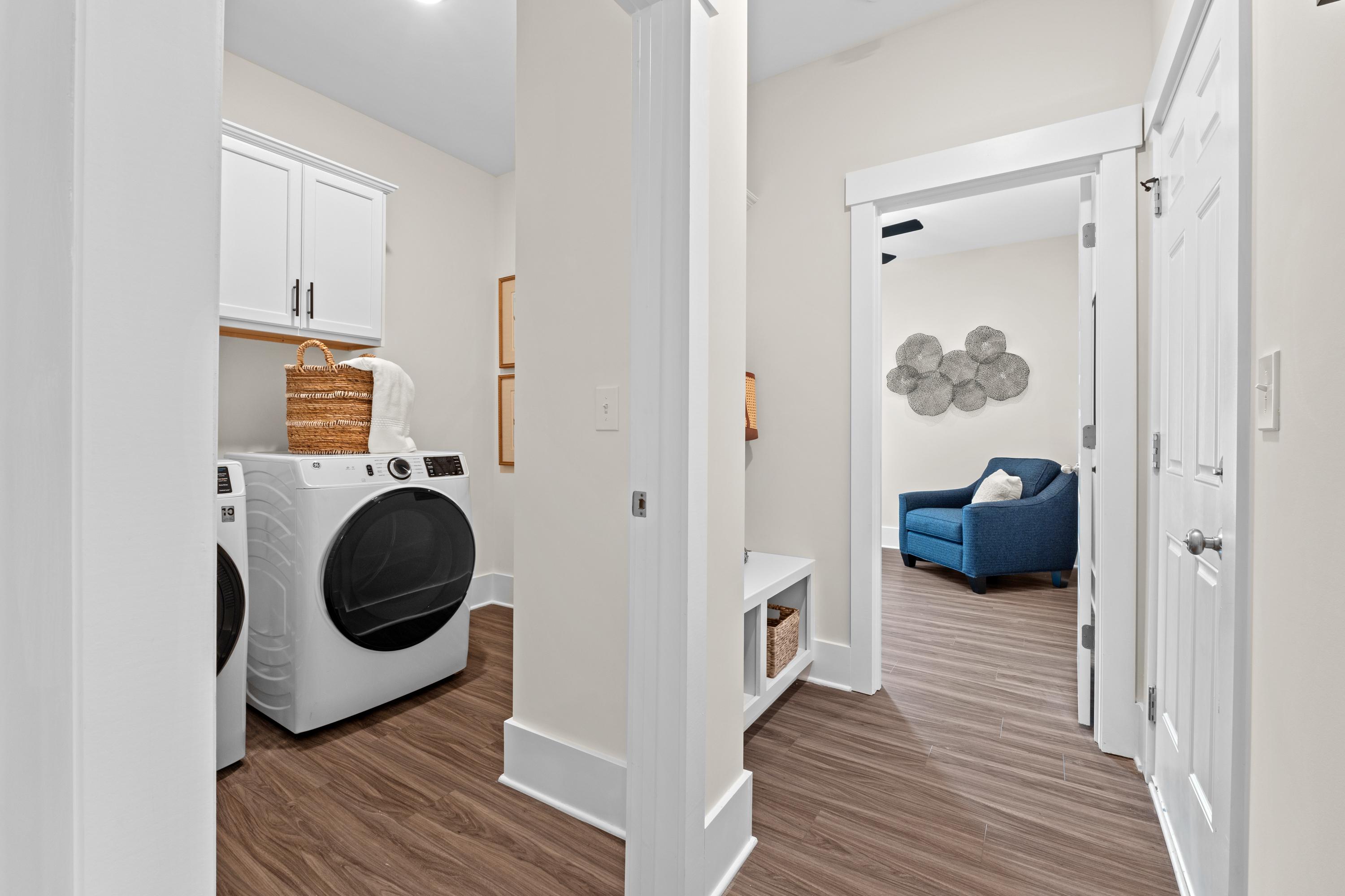 Spacious laundry room and mudroom at Ivy Hills in Toney, Alabama with white cabinets, washer-dryer, hardwood floors, blue accent chair