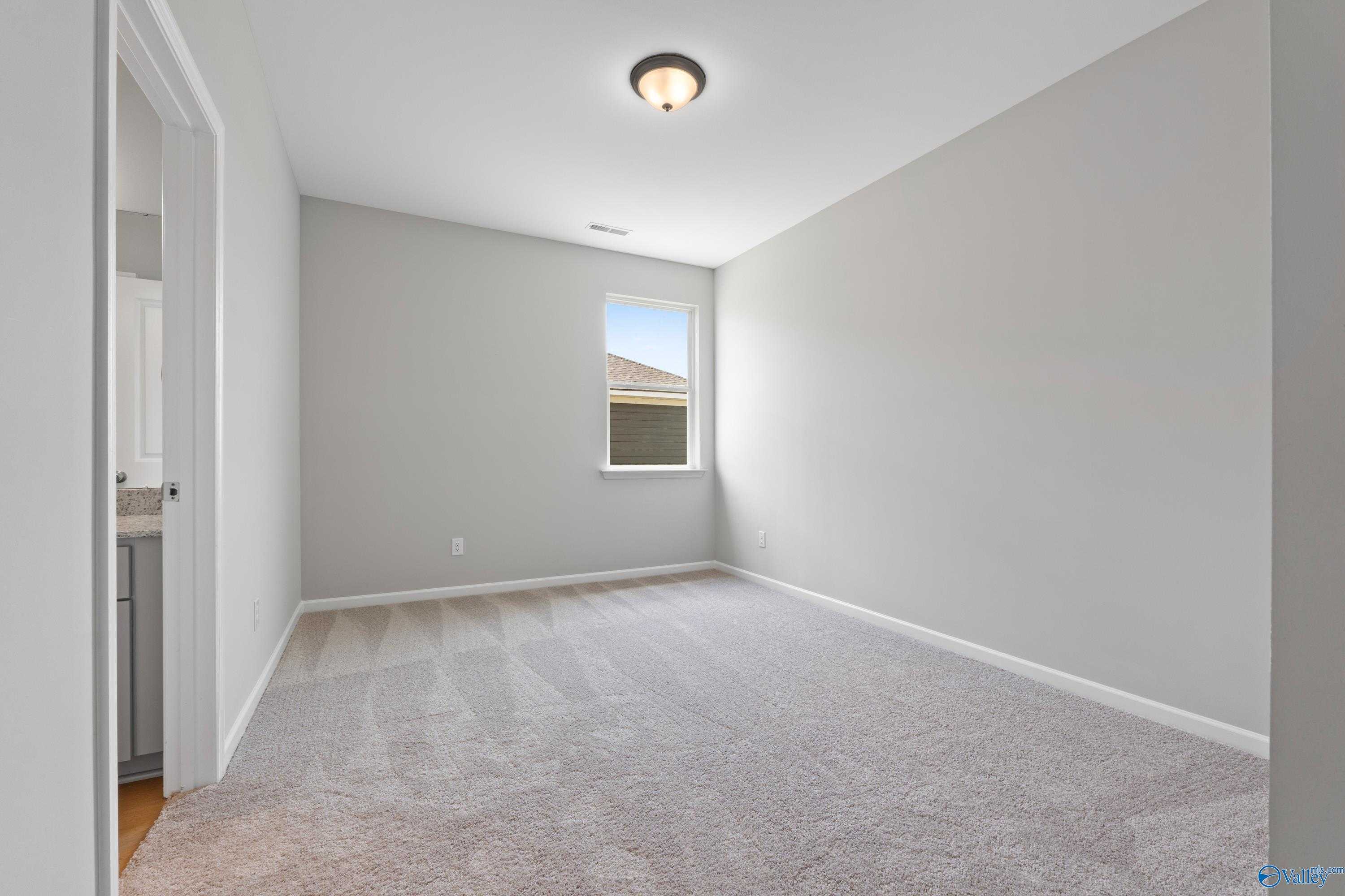 Bright empty secondary bedroom with light gray walls, beige carpet, and window in Davidson Homes The Orion, Athens Alabama
