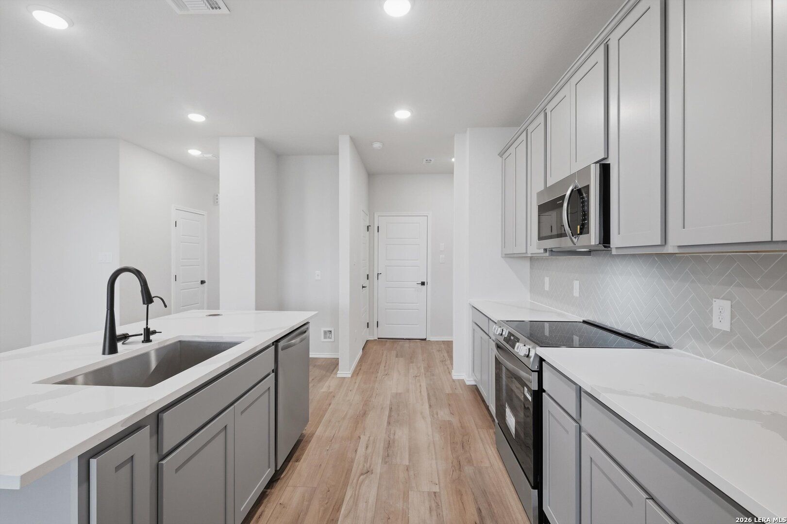 Modern kitchen featuring white quartz counters, gray shaker cabinets, stainless appliances, herringbone backsplash in Davidson Homes The Blanco C, San Antonio