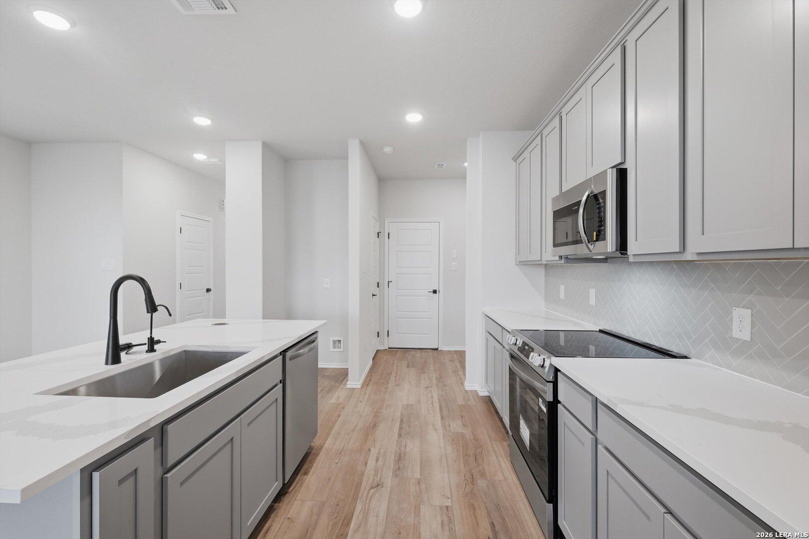Modern kitchen featuring white quartz counters, gray shaker cabinets, stainless appliances, herringbone backsplash in Davidson Homes The Blanco C, San Antonio