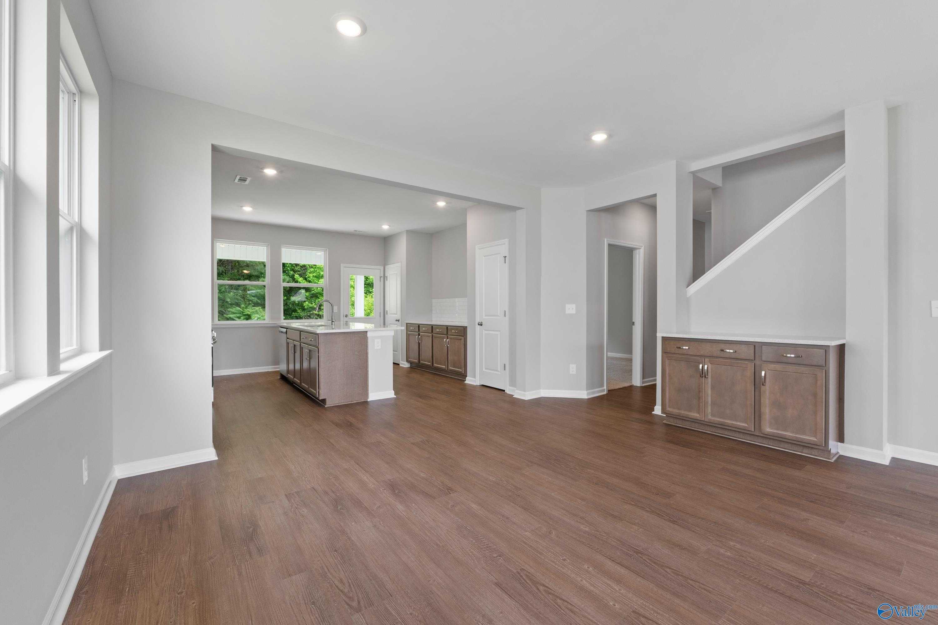 Open-concept living area with kitchen island, hardwood floors, white cabinets, and staircase in Davidson Homes The Stella, Hazel Green, Alabama
