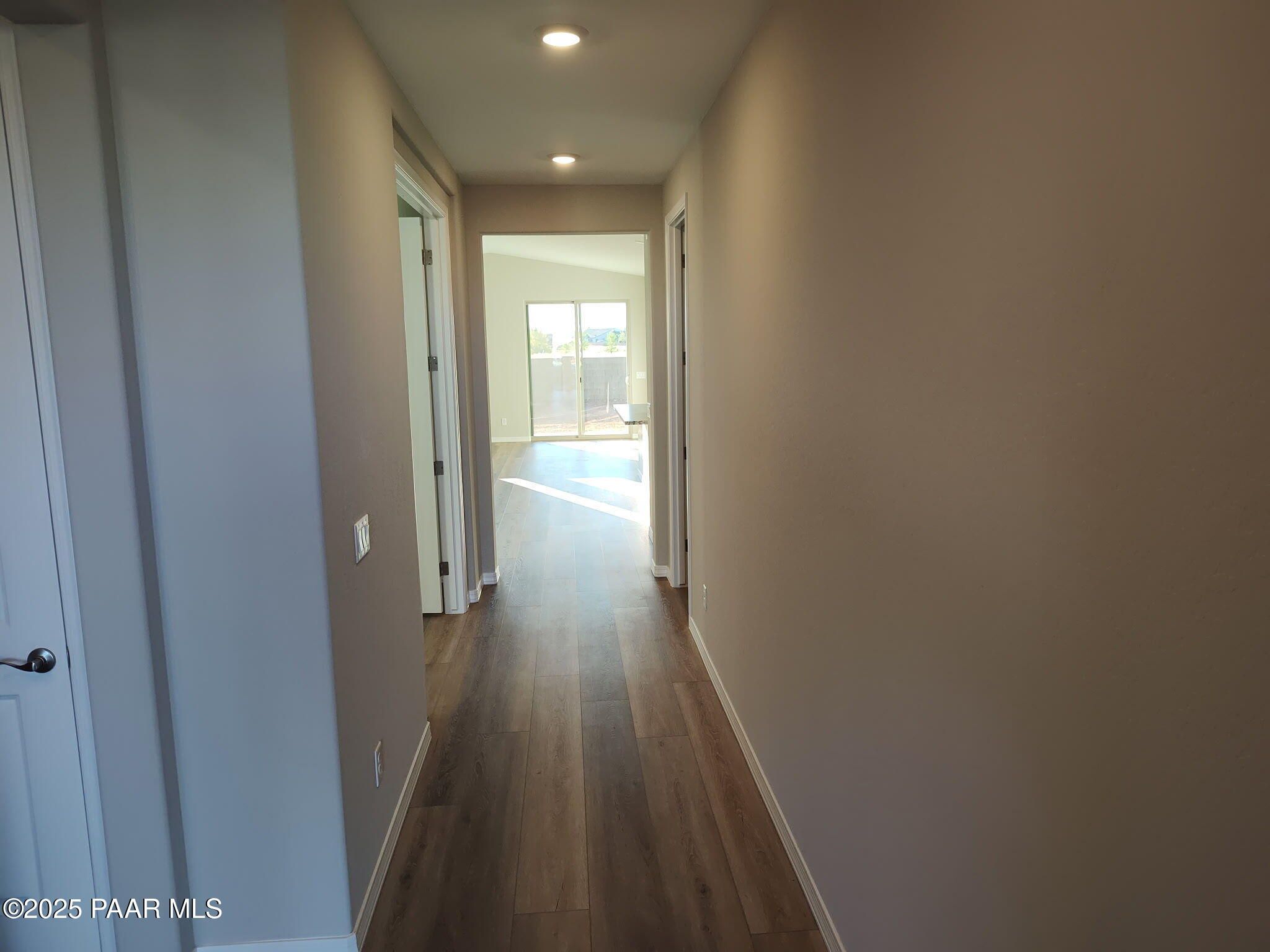 Bright hallway with light oak laminate floors, neutral beige walls, and doors leading to sunlit great room in The Frontier C, Prescott Valley, Arizona