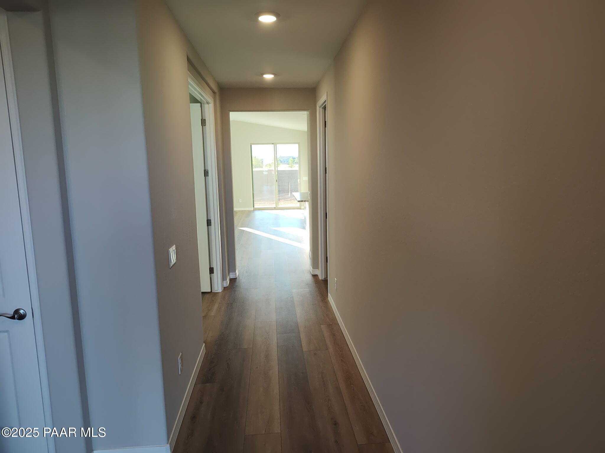 Bright hallway with light oak laminate floors, neutral beige walls, and doors leading to sunlit great room in The Frontier C, Prescott Valley, Arizona