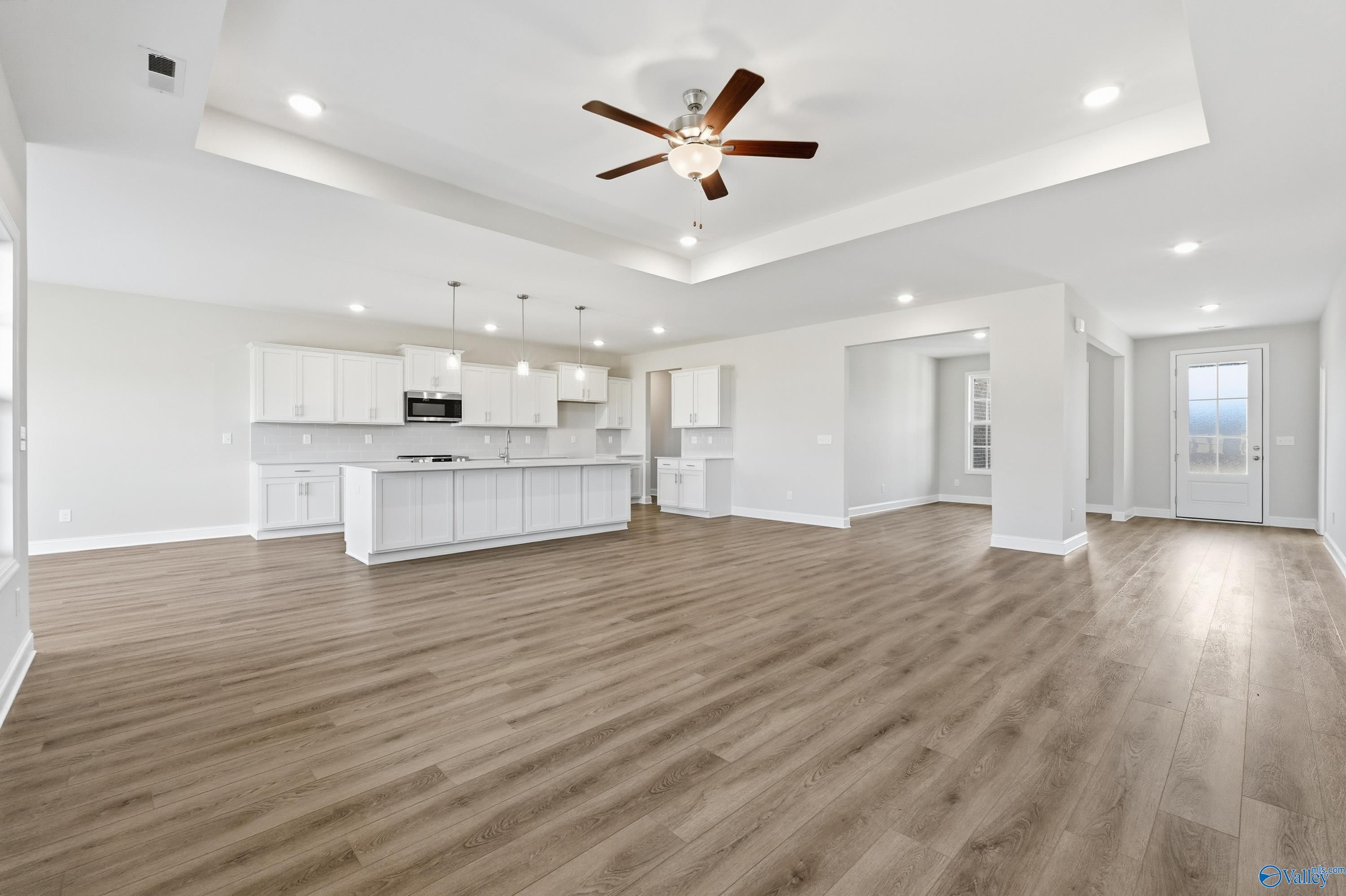 Open-concept great room with ceiling fan, white cabinetry, kitchen island, and hardwood floors in Davidson Homes Finleigh, Harvest AL
