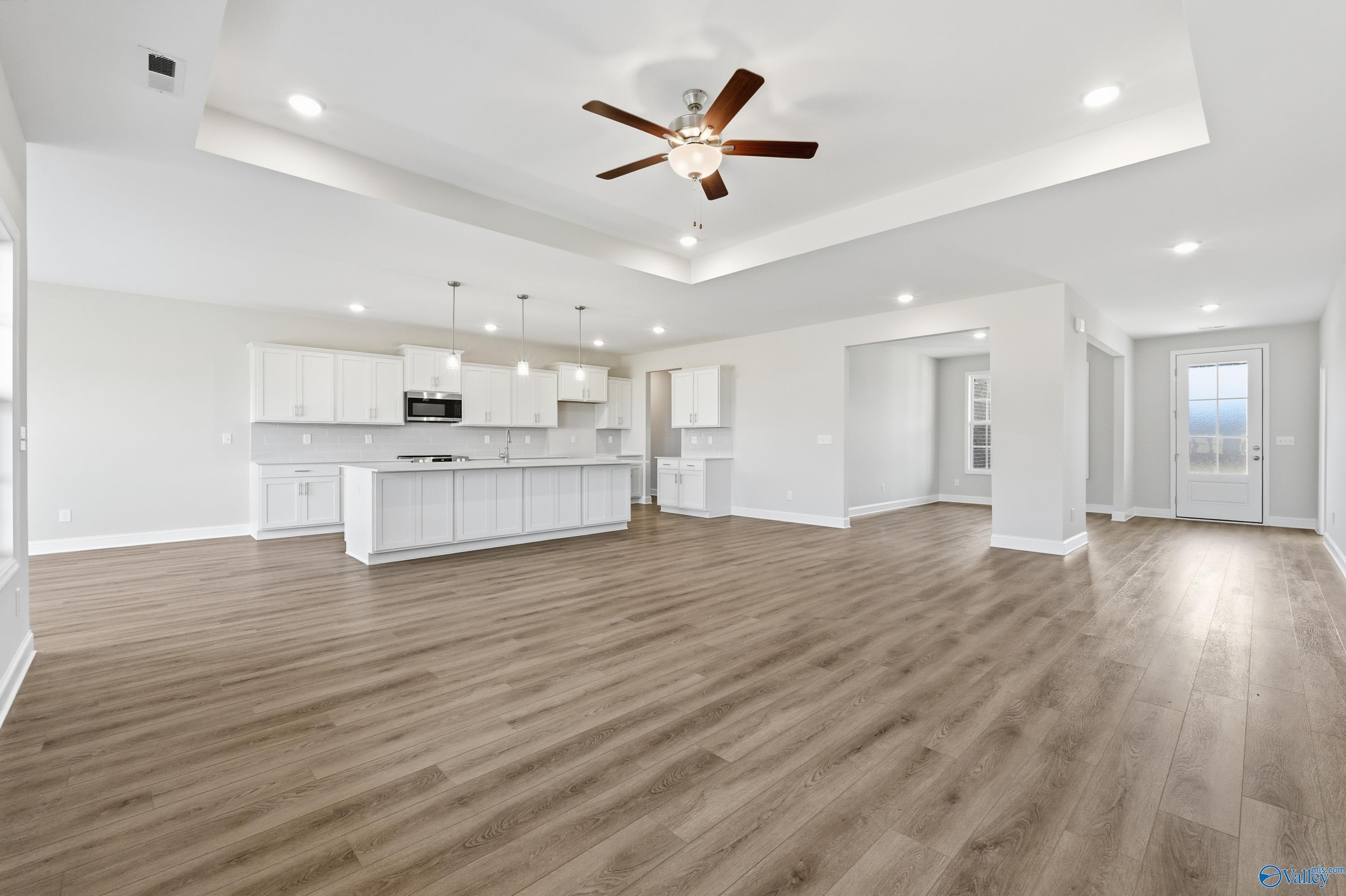 Open-concept great room with ceiling fan, white cabinetry, kitchen island, and hardwood floors in Davidson Homes Finleigh, Harvest AL