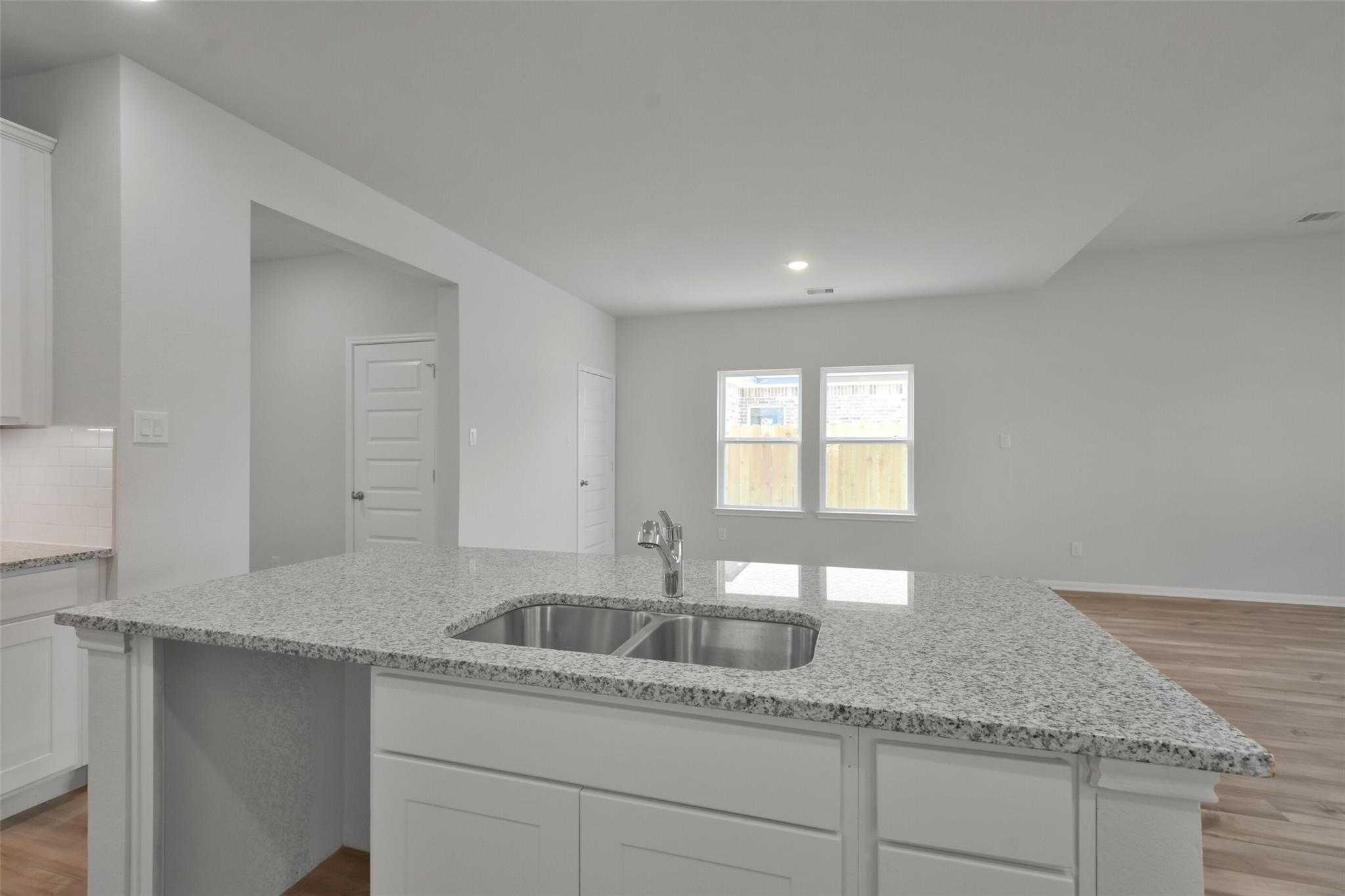 Modern kitchen with granite island, double sink, white cabinets, and open layout in Davidson Homes The Tierra A, Dayton, Texas