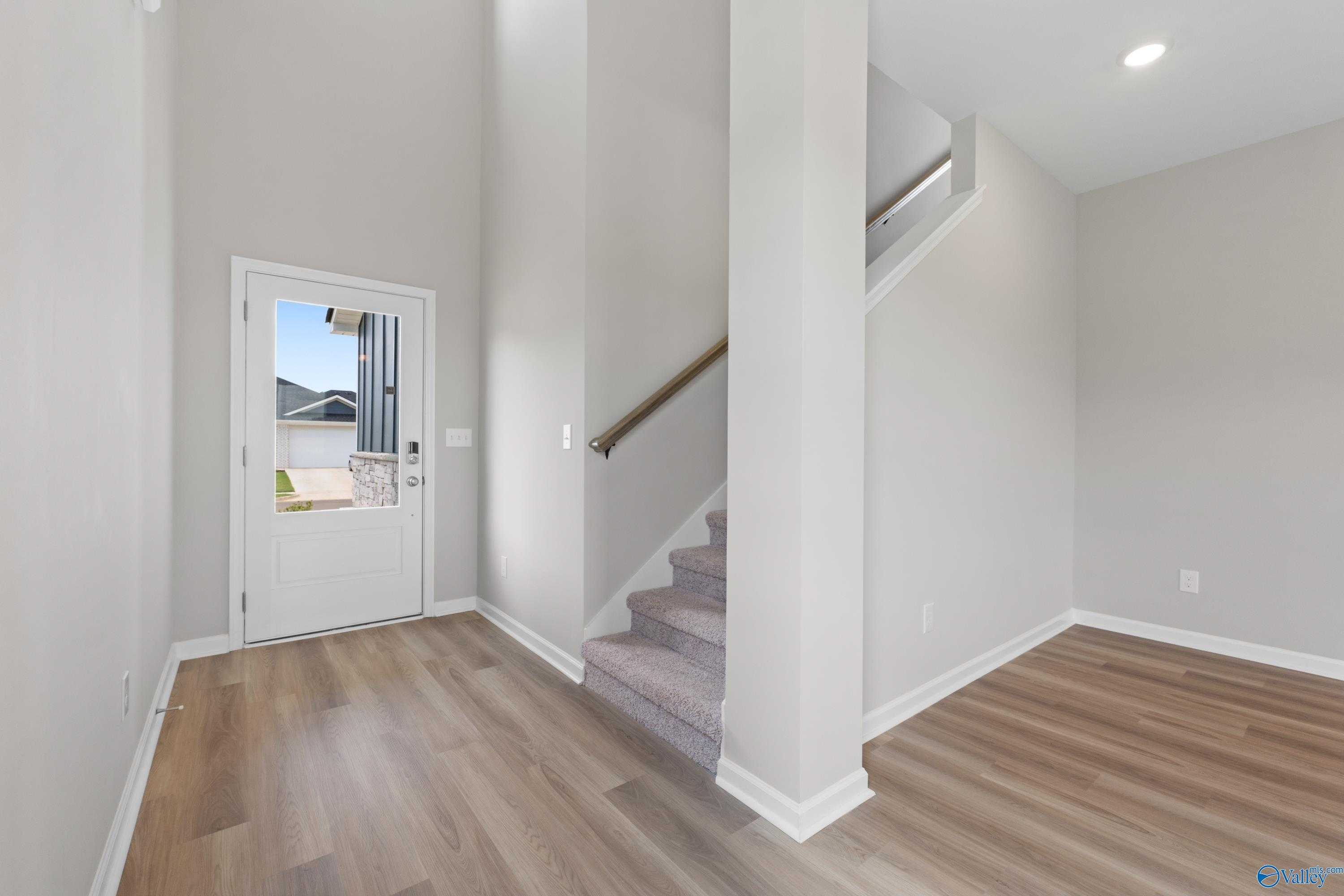 Bright two-story foyer with sweeping carpeted staircase and sunlit front door in Evermore Homes The Augusta, Madison, Alabama