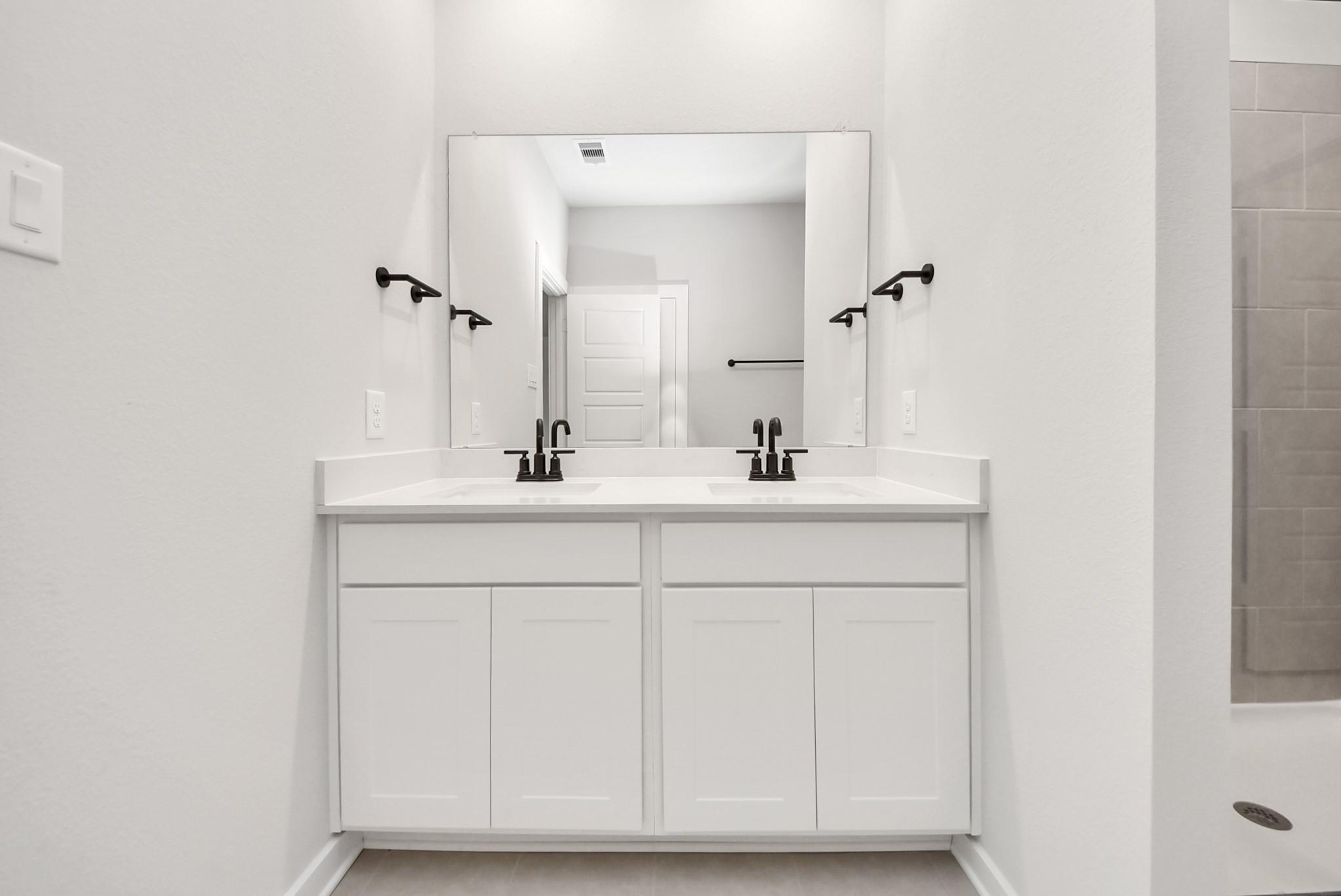 Modern double vanity with white cabinets and matte black fixtures in The Daphne F home at Sundance Cove, Crosby, Texas.
