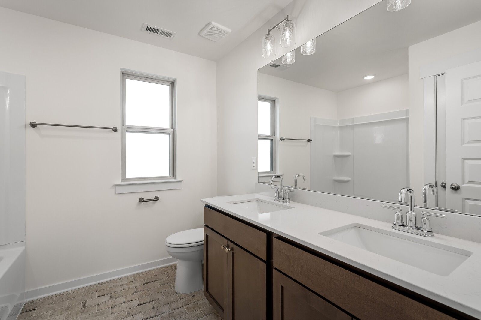 Modern bathroom with double vanity, white quartz counters, brown cabinets, glass shower, and brick tile floor in Davidson Homes Willow C, Gallatin, TN