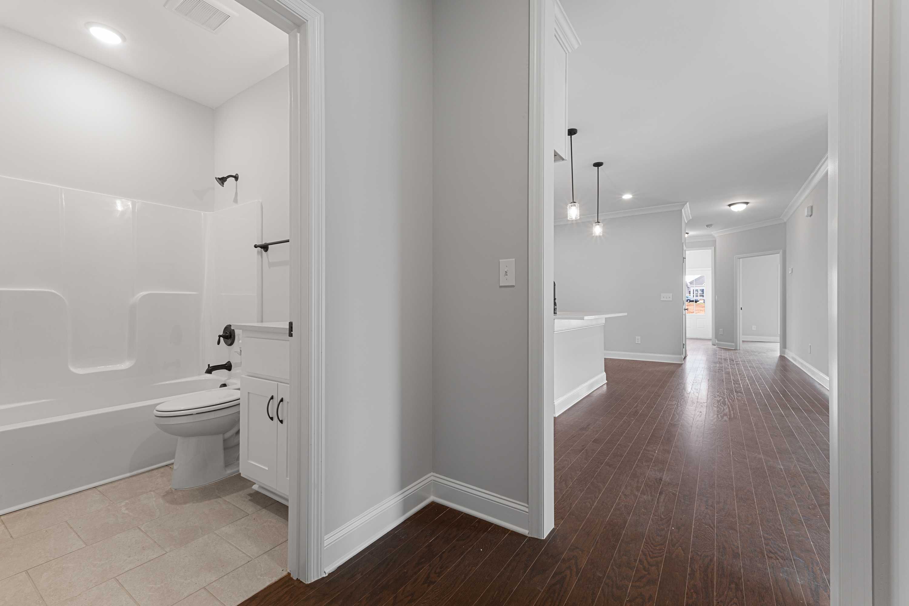 Master bathroom in The Copeland with white tub, vanity, toilet, and adjacent hardwood hallway by Davidson Homes