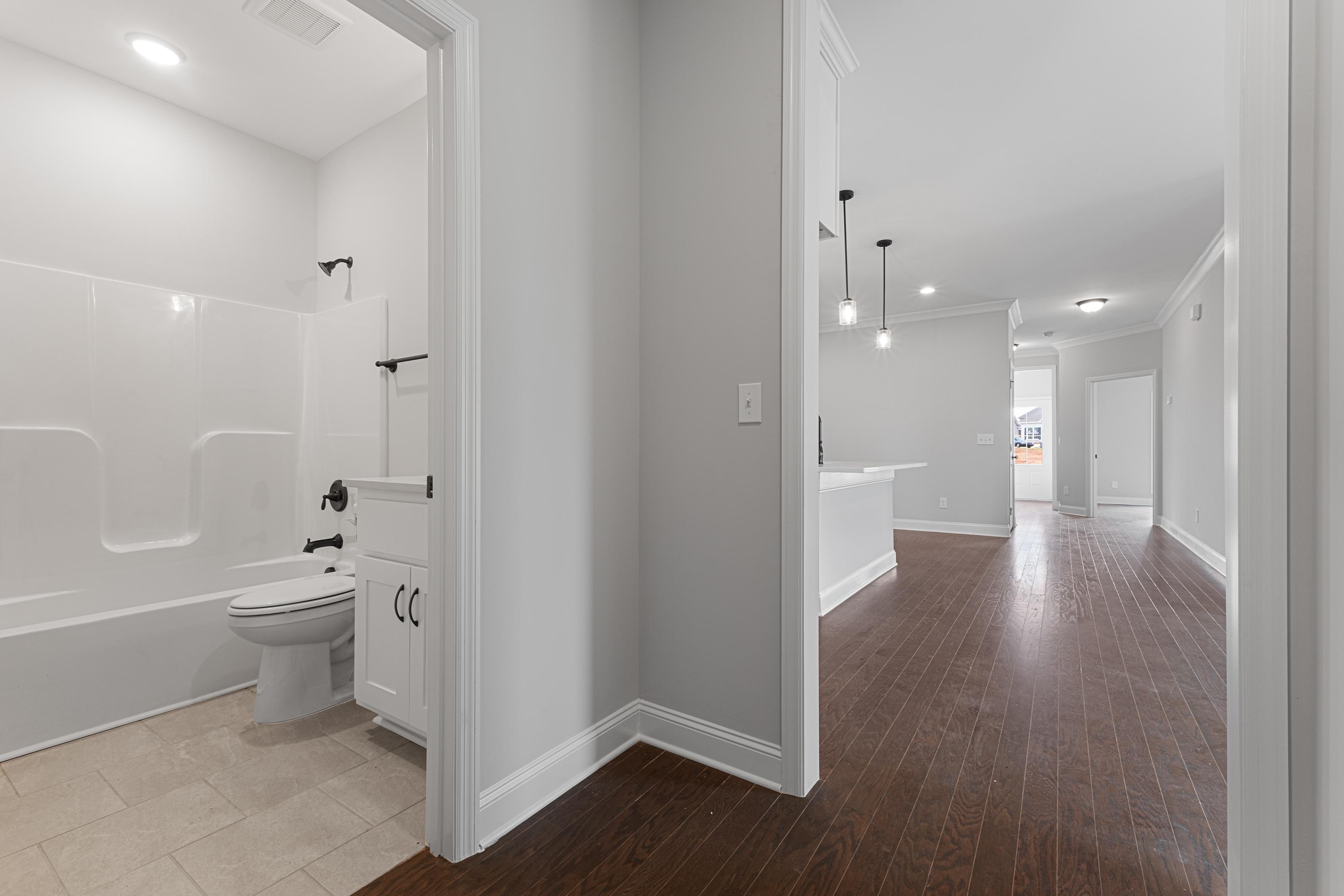 Master bathroom in The Copeland featuring white tub, walk-in shower, vanity, and adjacent hallway with hardwood floors