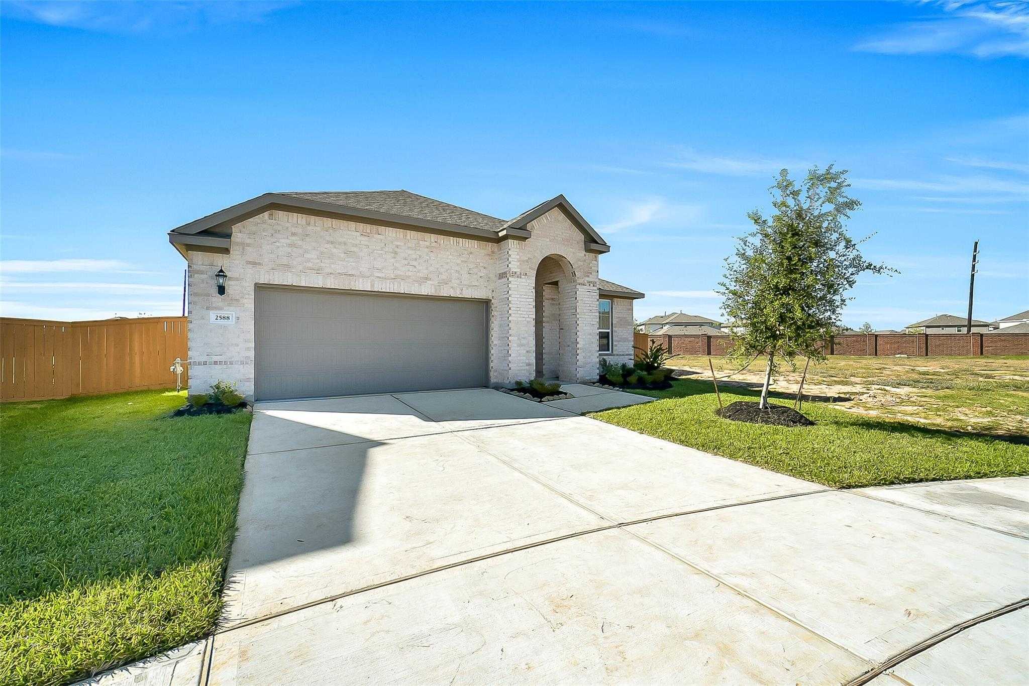 Modern single-story brick home with arched entry, two-car garage, driveway, and lush lawn in Sunterra, Katy, Texas