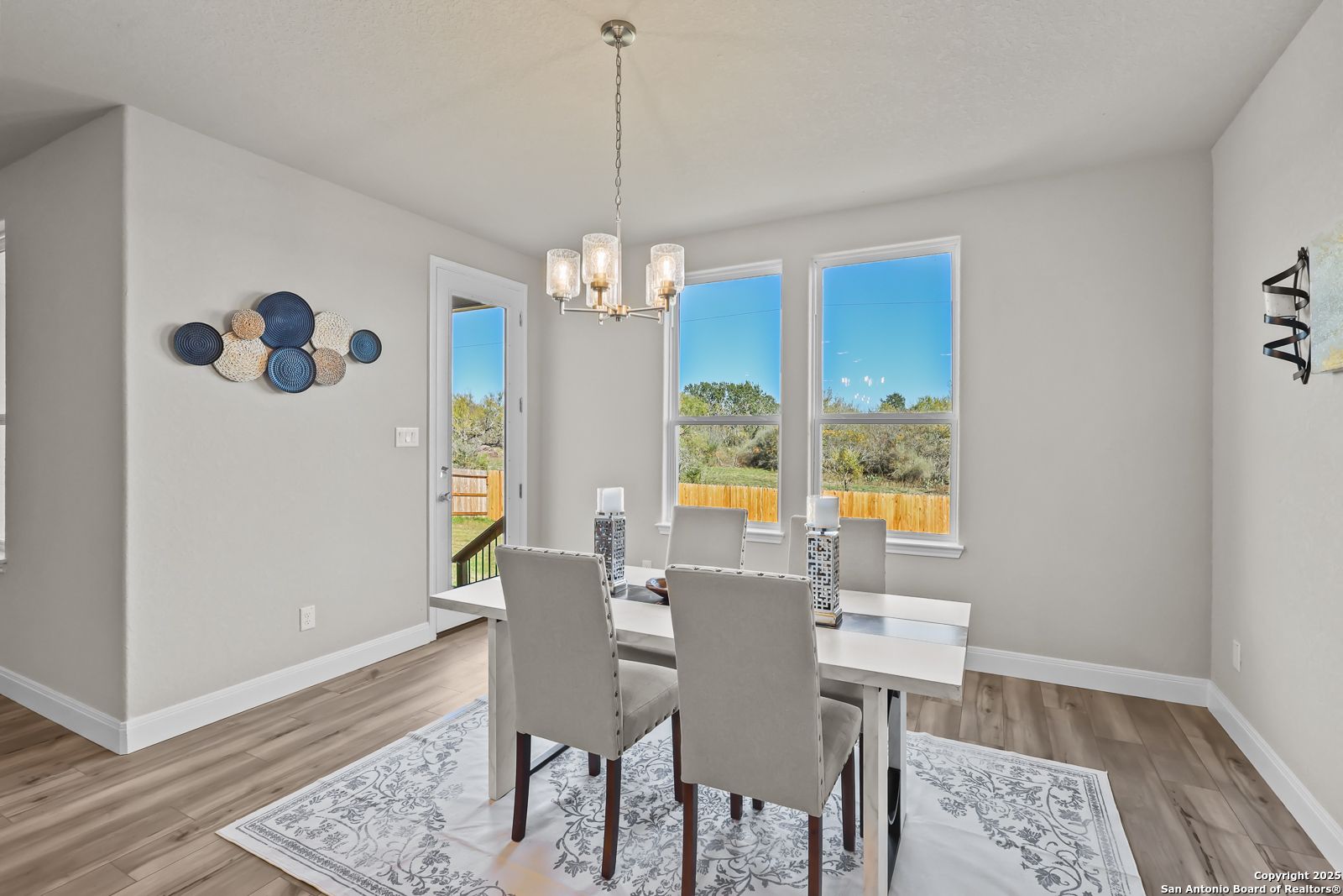 Elegant dining room with modern chandelier, white table, upholstered chairs, and backyard view in The Jennings G, Castroville, Texas