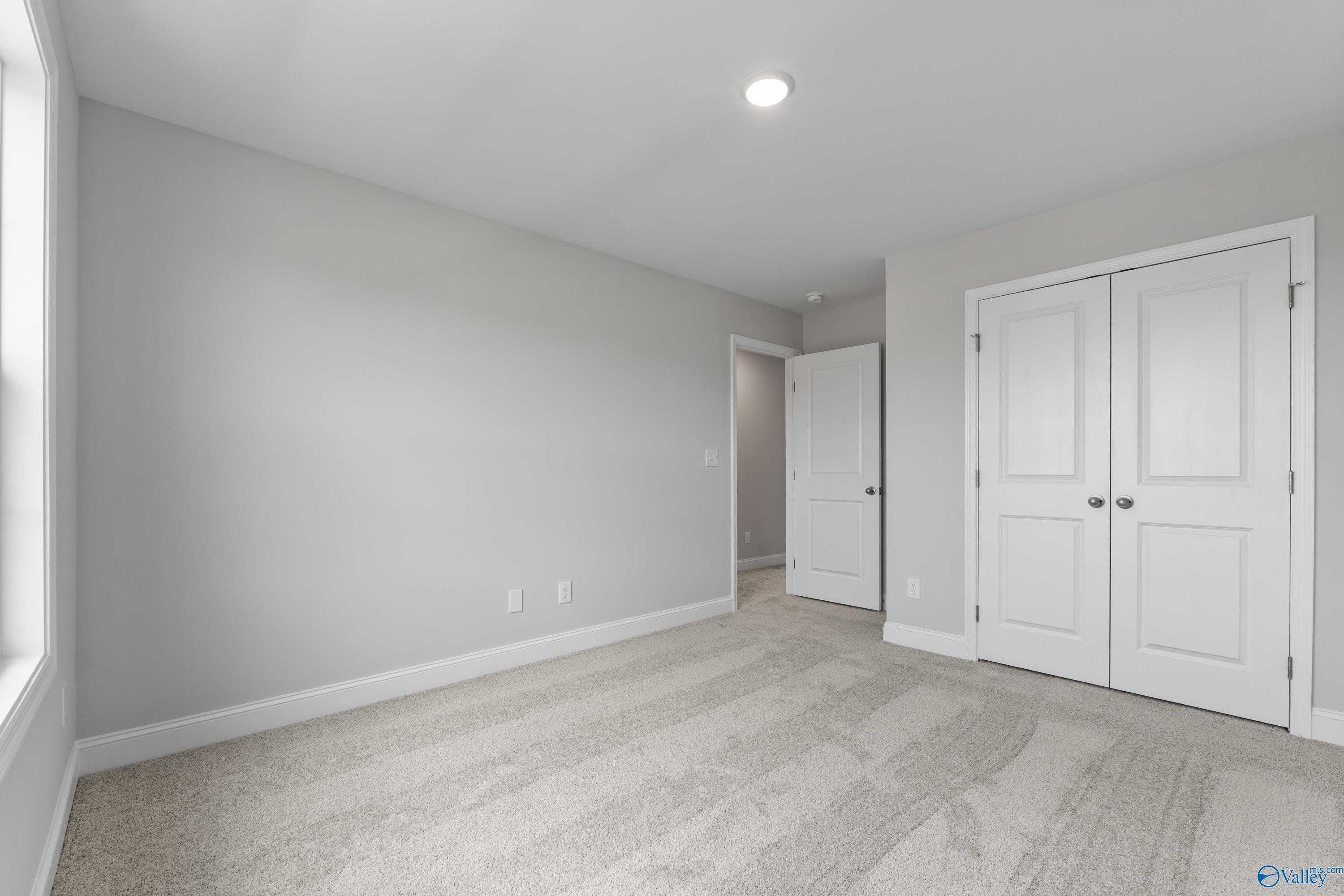 Light gray master bedroom with white double closet doors, carpeted floor, and large window in Davidson Homes The Madison A, Toney, Alabama