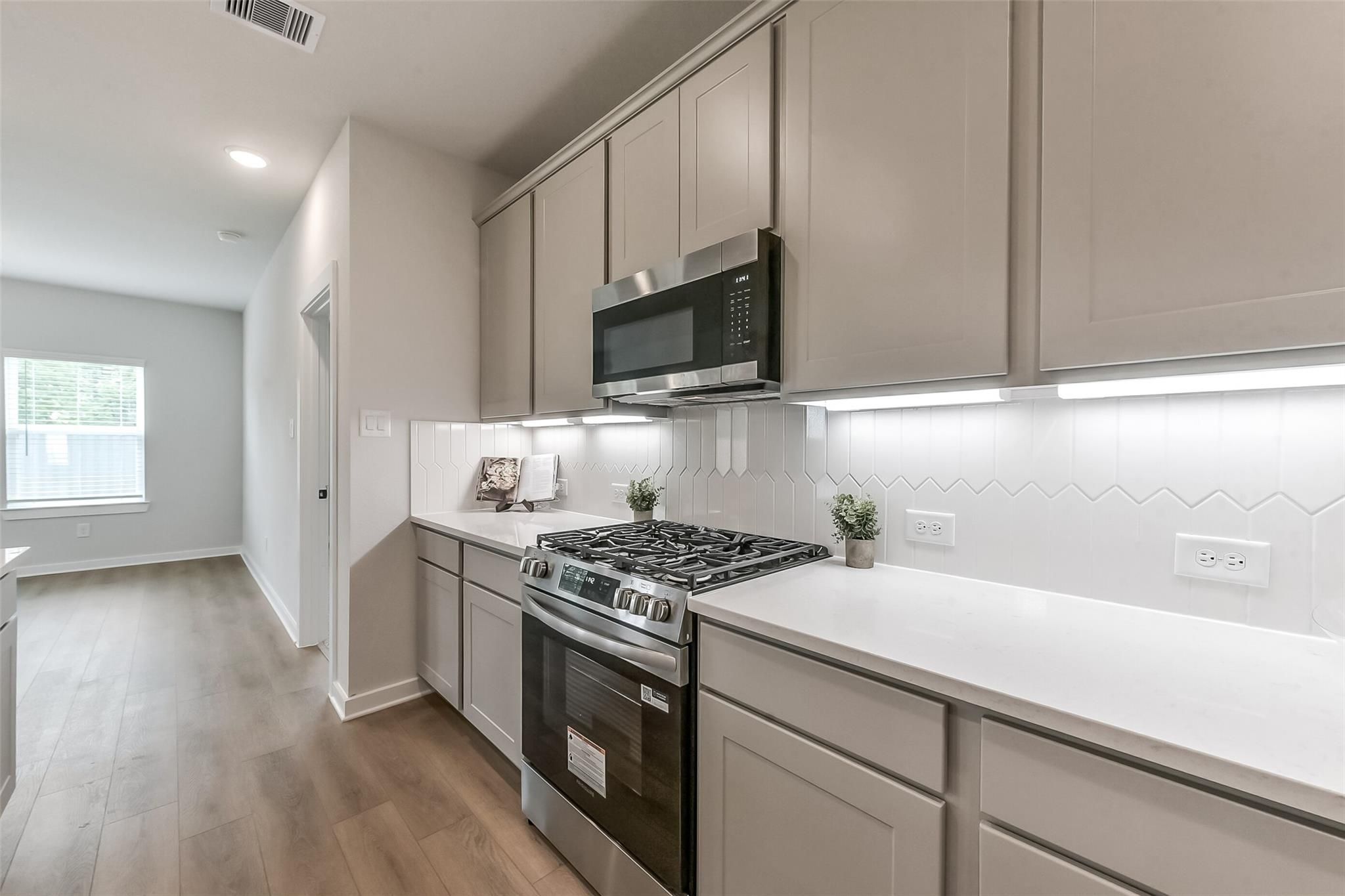 Modern kitchen featuring white quartz counters, stainless gas range, herringbone backsplash, and beige cabinets in The Everett C, Crosby, Texas