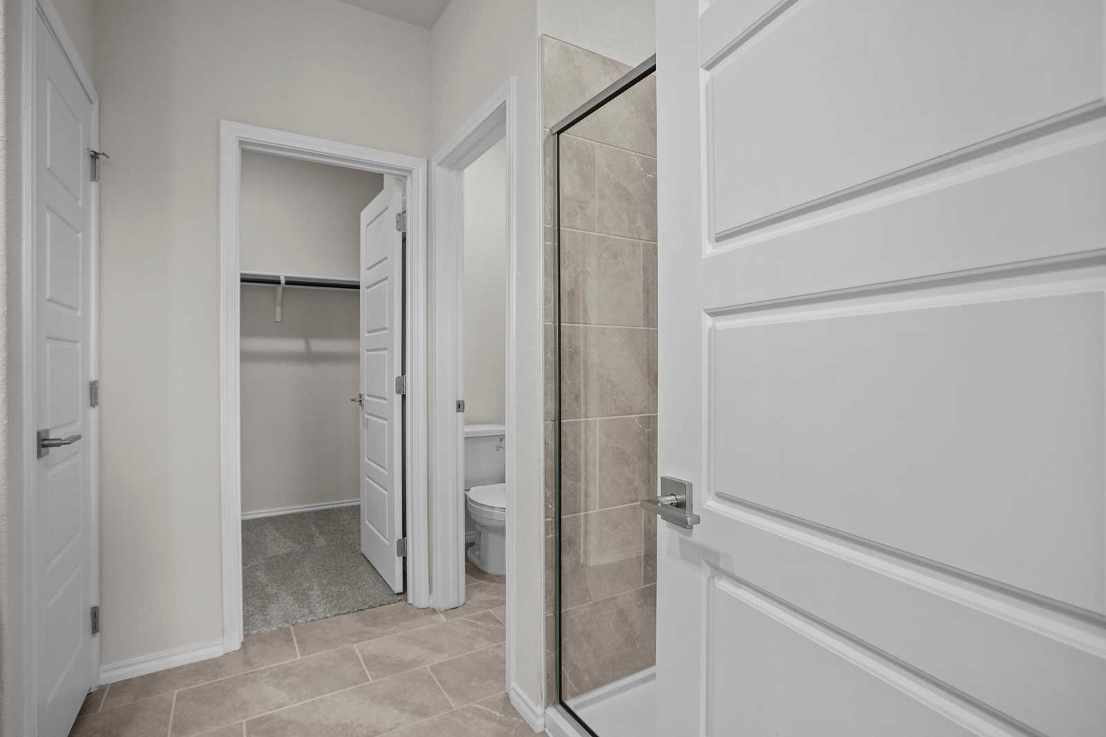 Modern master bathroom with glass shower, white toilet, and adjacent walk-in closet in The Redbud B, Josephine, Texas
