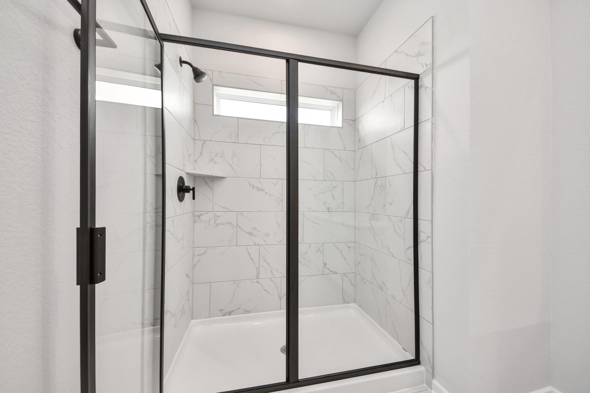 Modern walk-in shower with marble-look tile and black frame in The Sorrento E floor plan at Sundance Cove, Crosby, Texas.