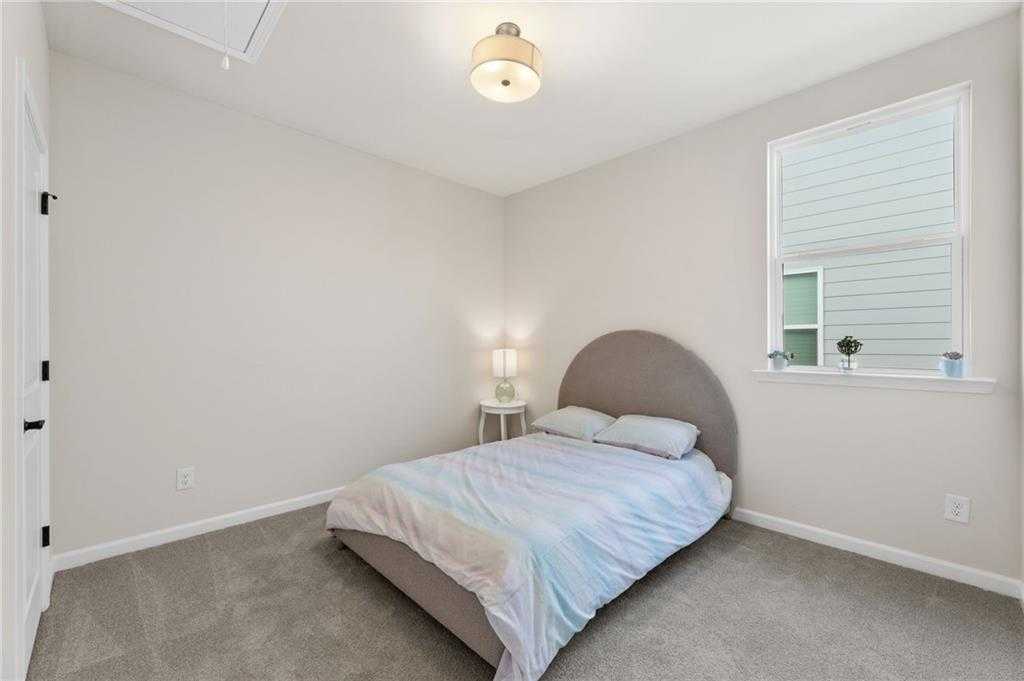 Cozy secondary bedroom with tufted gray headboard bed, rainbow duvet, nightstand lamp, and window in Davidson Homes The Daphne B, Loganville, GA