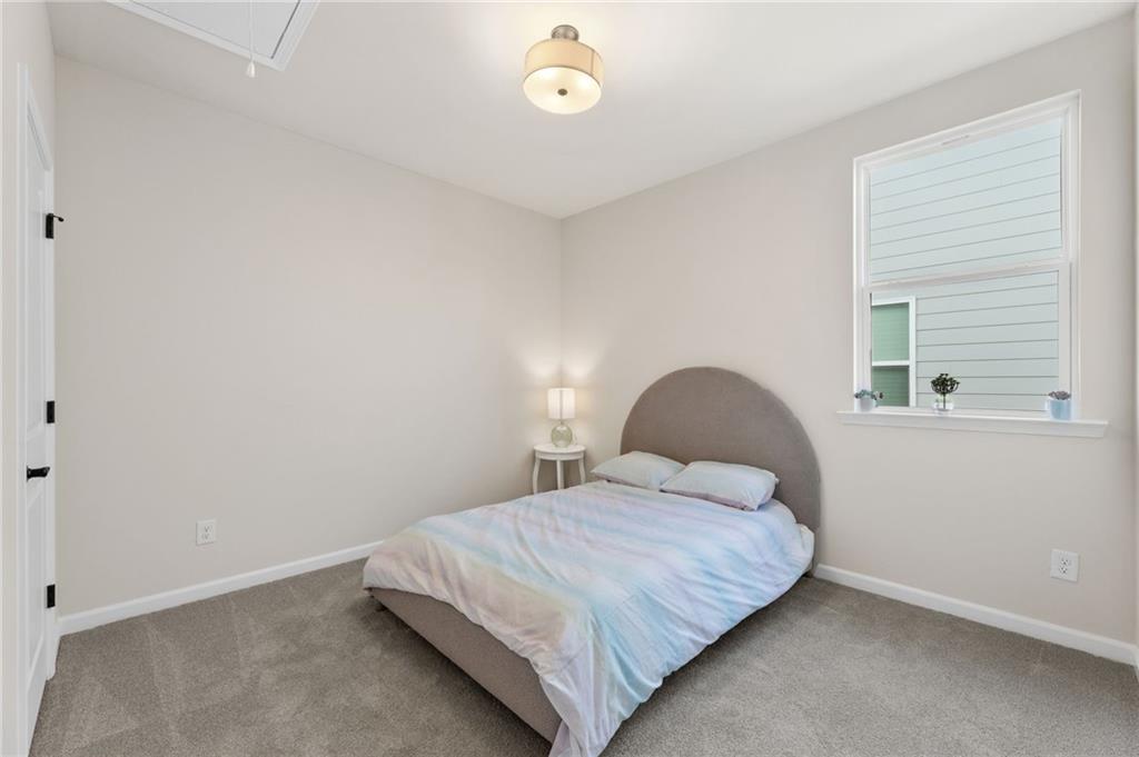 Cozy secondary bedroom with tufted gray headboard, colorful bedding, nightstand lamp, and large window in Davidson Homes The Daphne B, Loganville, GA