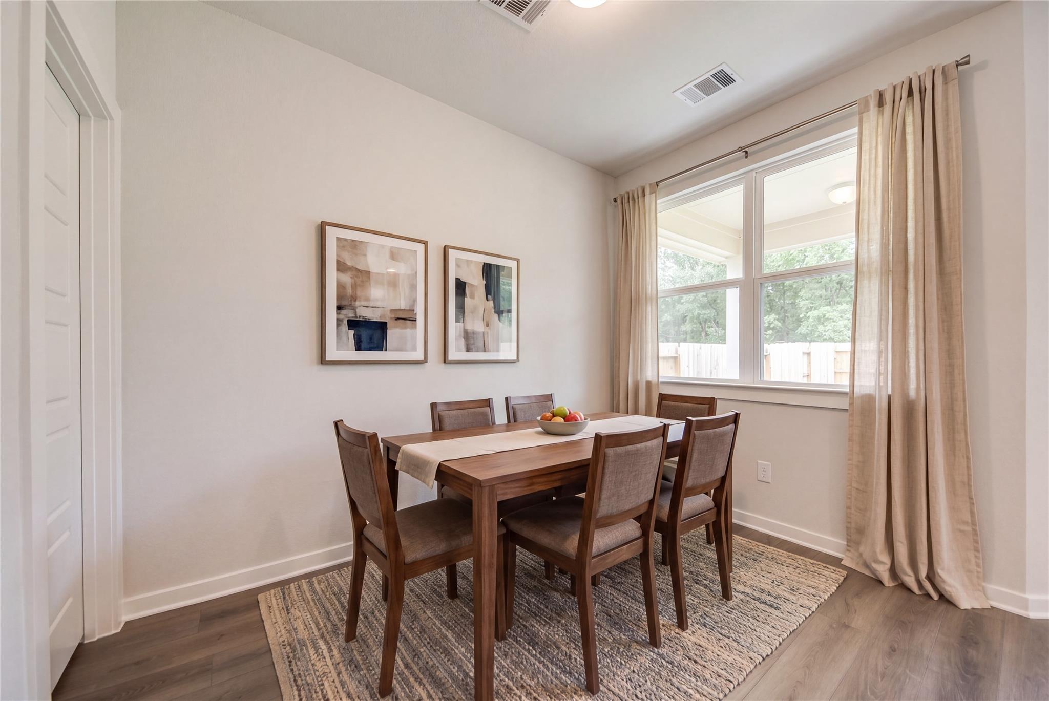 Bright dining room with wood table, upholstered chairs, and large window in Davidson Homes The Daphne F, Sundance Cove, Crosby, Texas
