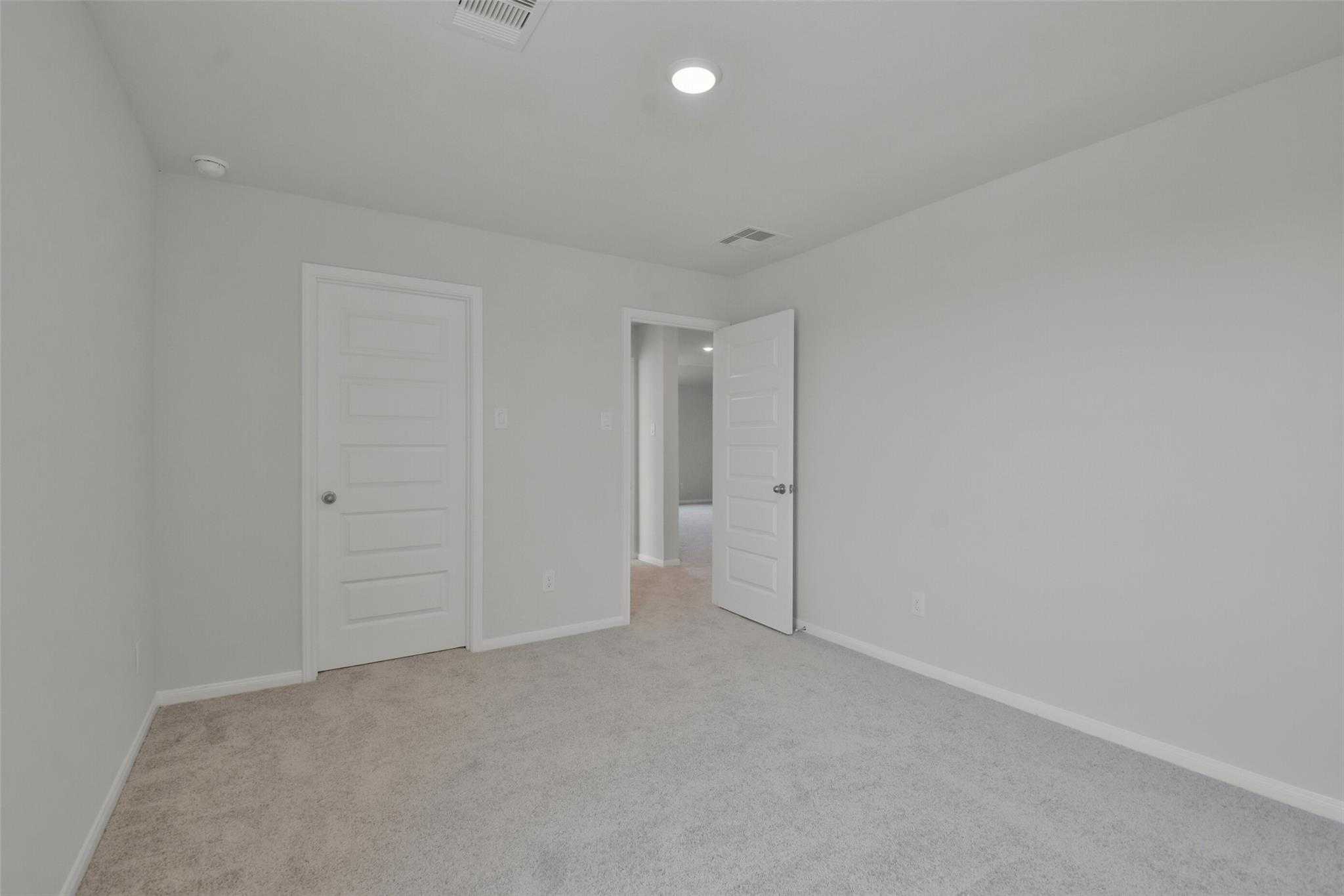 Spacious secondary bedroom with beige carpet, white walls, and open bath door in Davidson Homes The Tierra A, Dayton, Texas