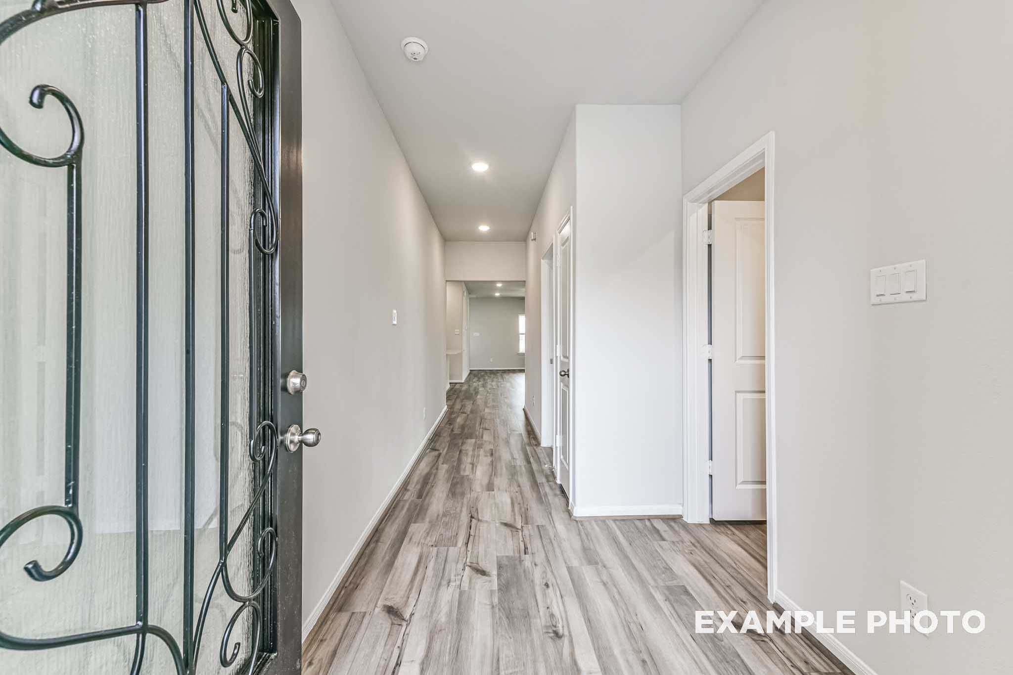 Spacious entry hallway in The Laguna A 3-car garage home with wrought iron door, white walls, and hardwood floors