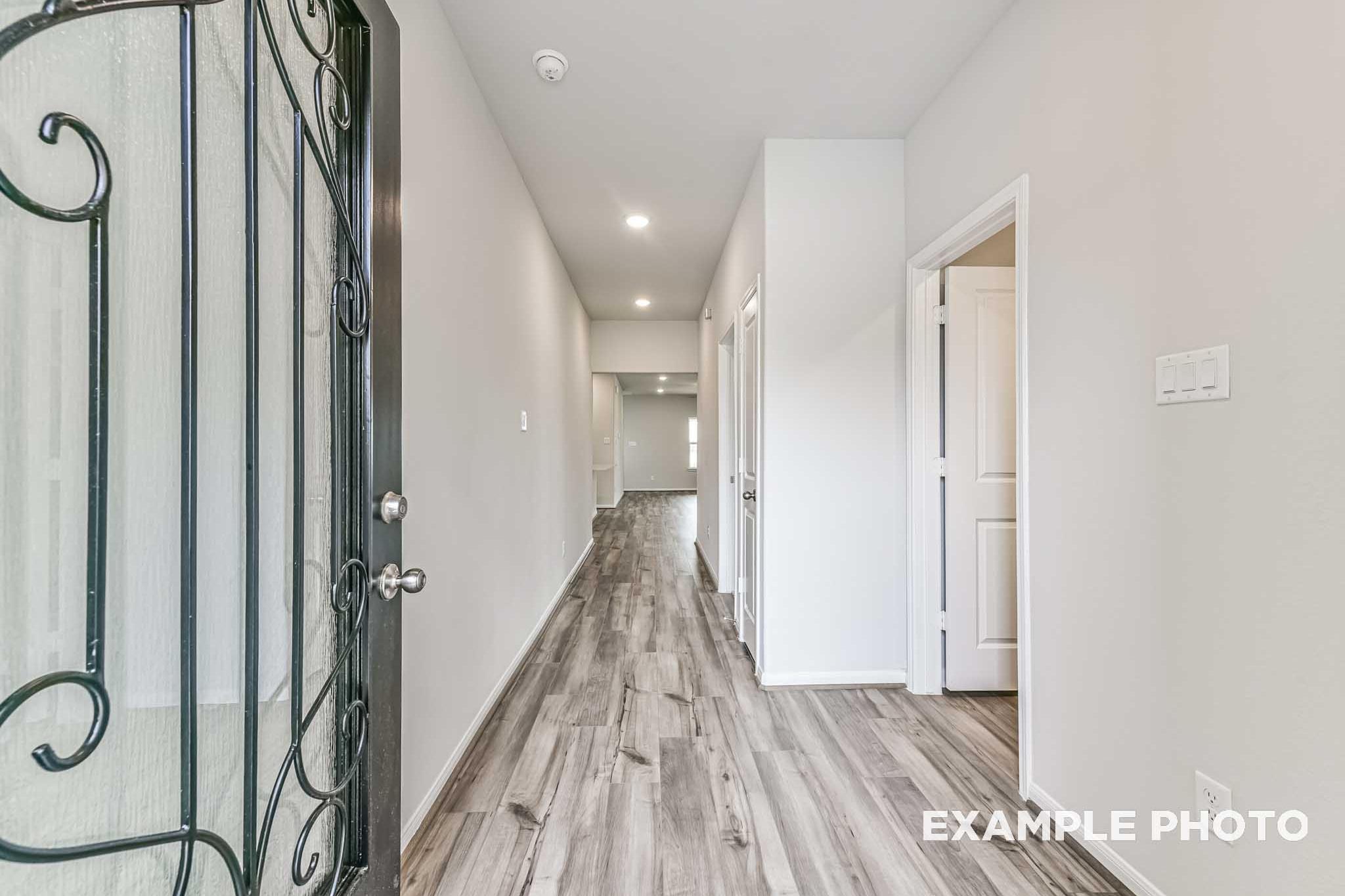 Spacious entry hallway in The Laguna A 3-car garage home with wrought iron door, white walls, and hardwood floors