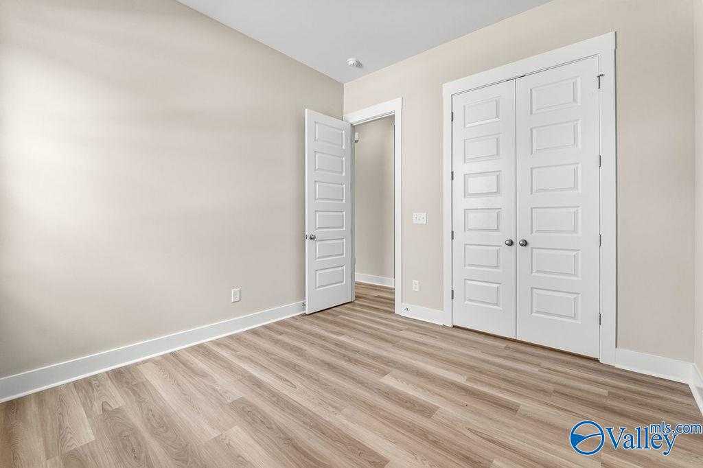 Spacious empty bedroom with beige walls, hardwood floors, double doors, and open doorway in Evermore Homes The Oxford, Owens Cross Roads, Alabama