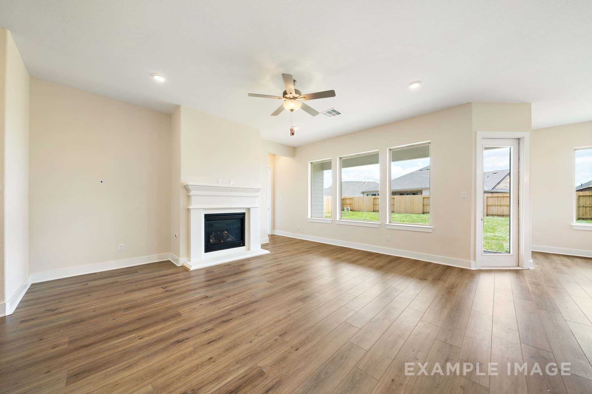 Spacious open-concept living room in The Diana C home with white fireplace, hardwood floors, and large windows overlooking backyard