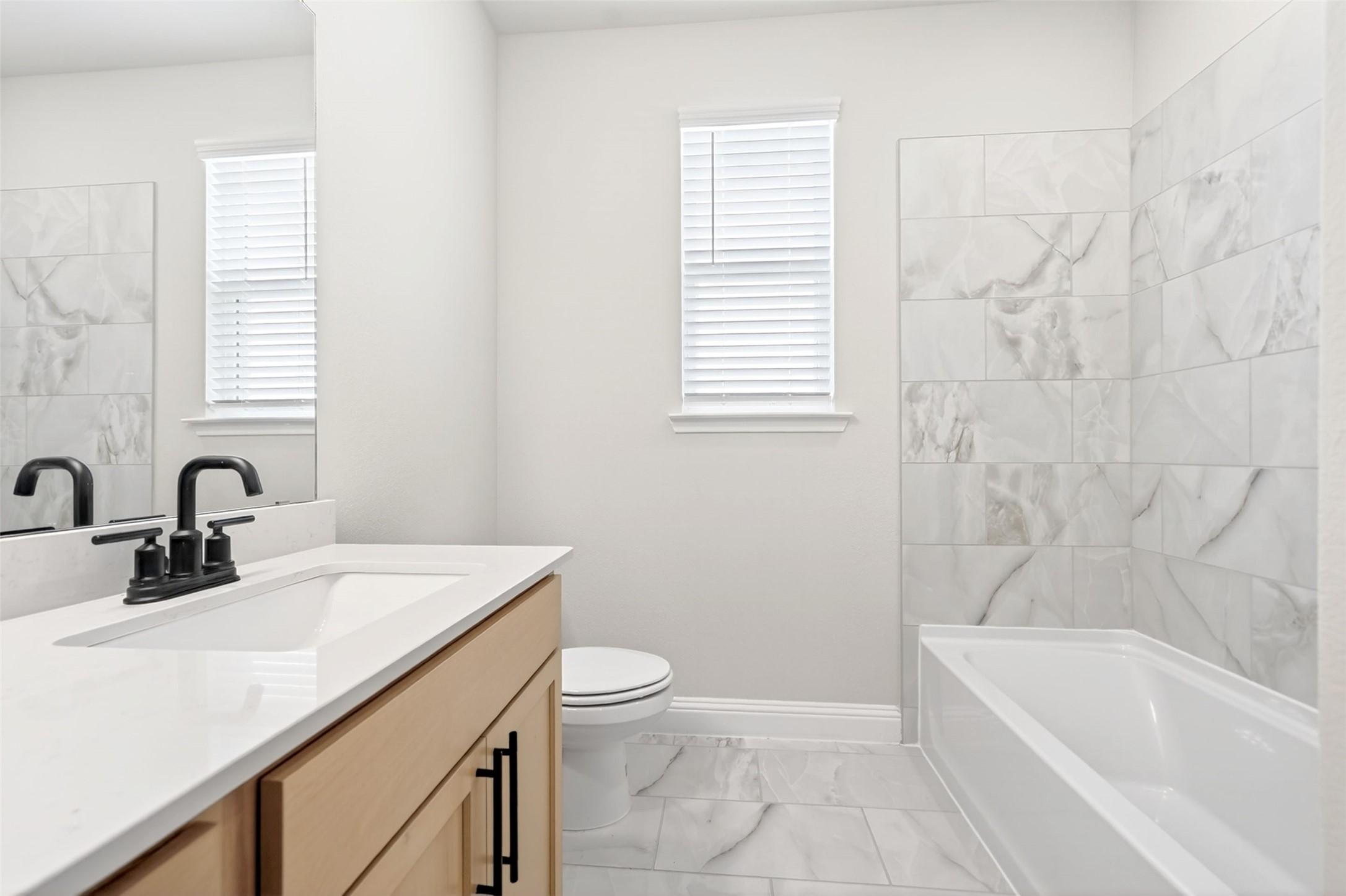 Modern bathroom with marble-style tile shower and light wood vanity in The Holly C floor plan, Parks at Foster Crossing.
