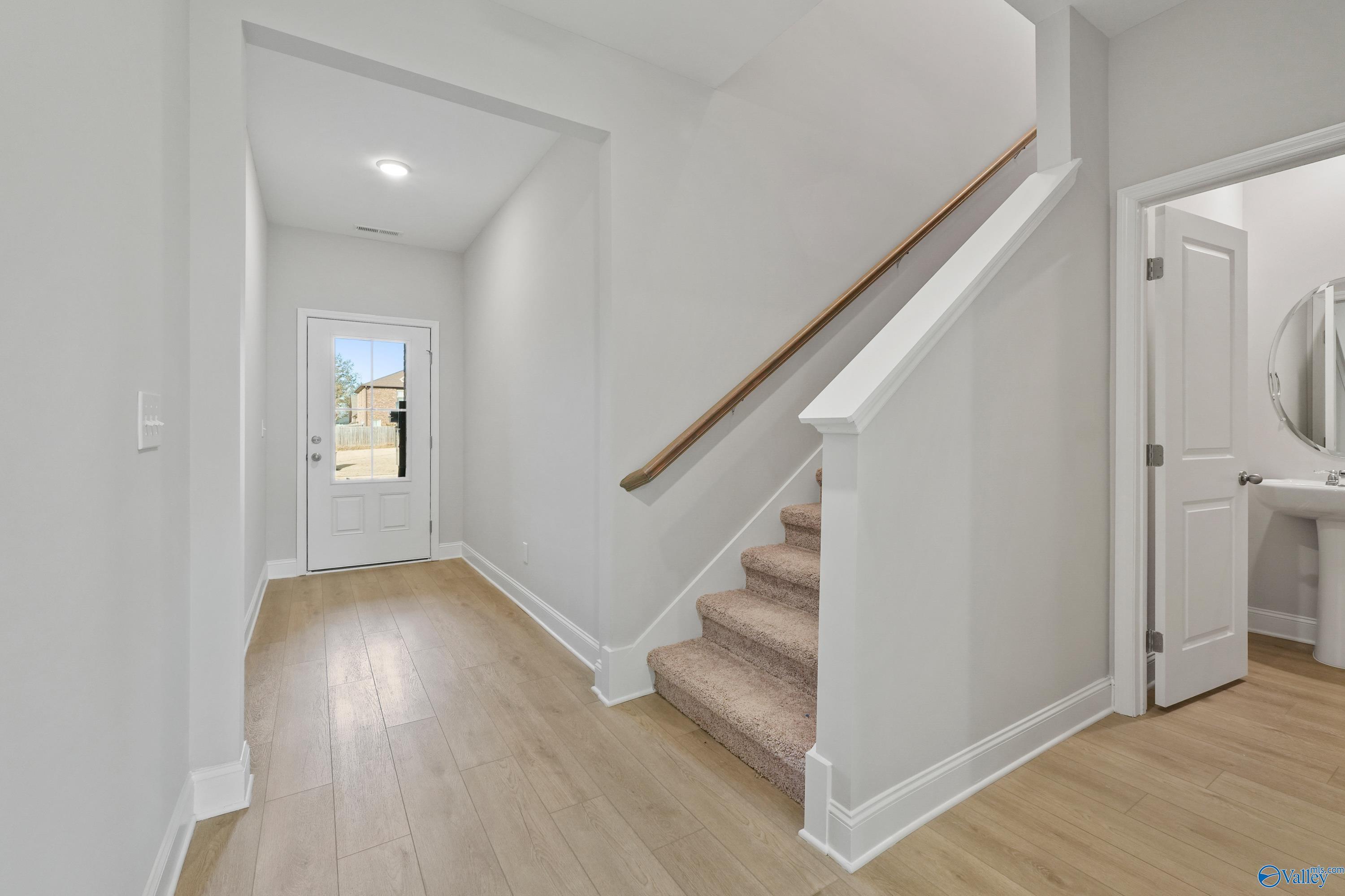 Bright entry foyer with light wood floors, carpeted staircase, and powder room in Davidson Homes The Camden B, Pavilion Huntsville AL