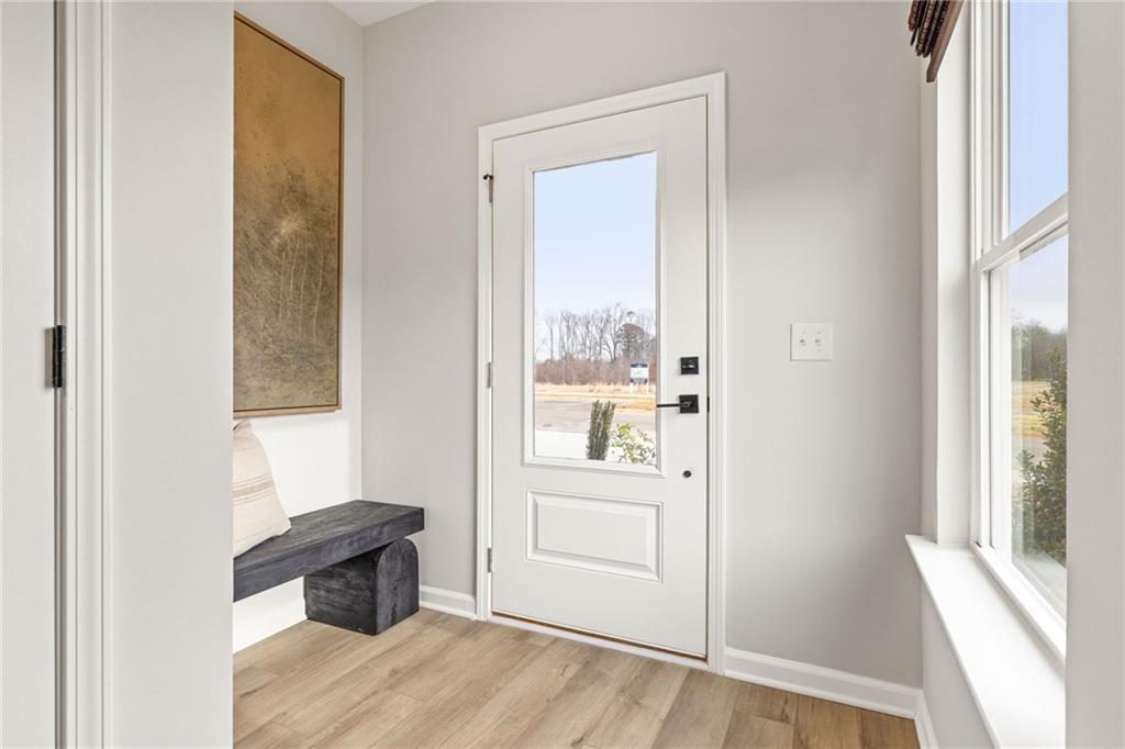Bright entryway with modern white front door, wood-look flooring, and bench in The Rabun B home at The Bluffs, Canton, GA.