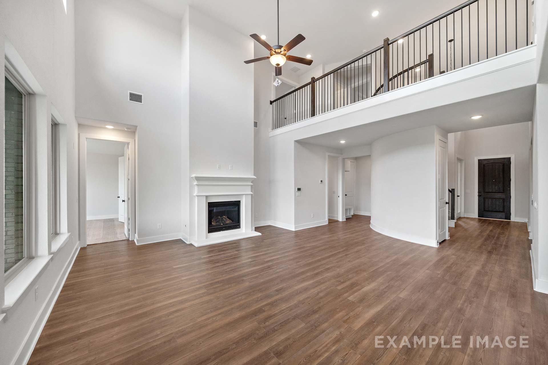 Spacious two-story living room in The Victoria home design with gas fireplace, balcony overlook, and hardwood floors