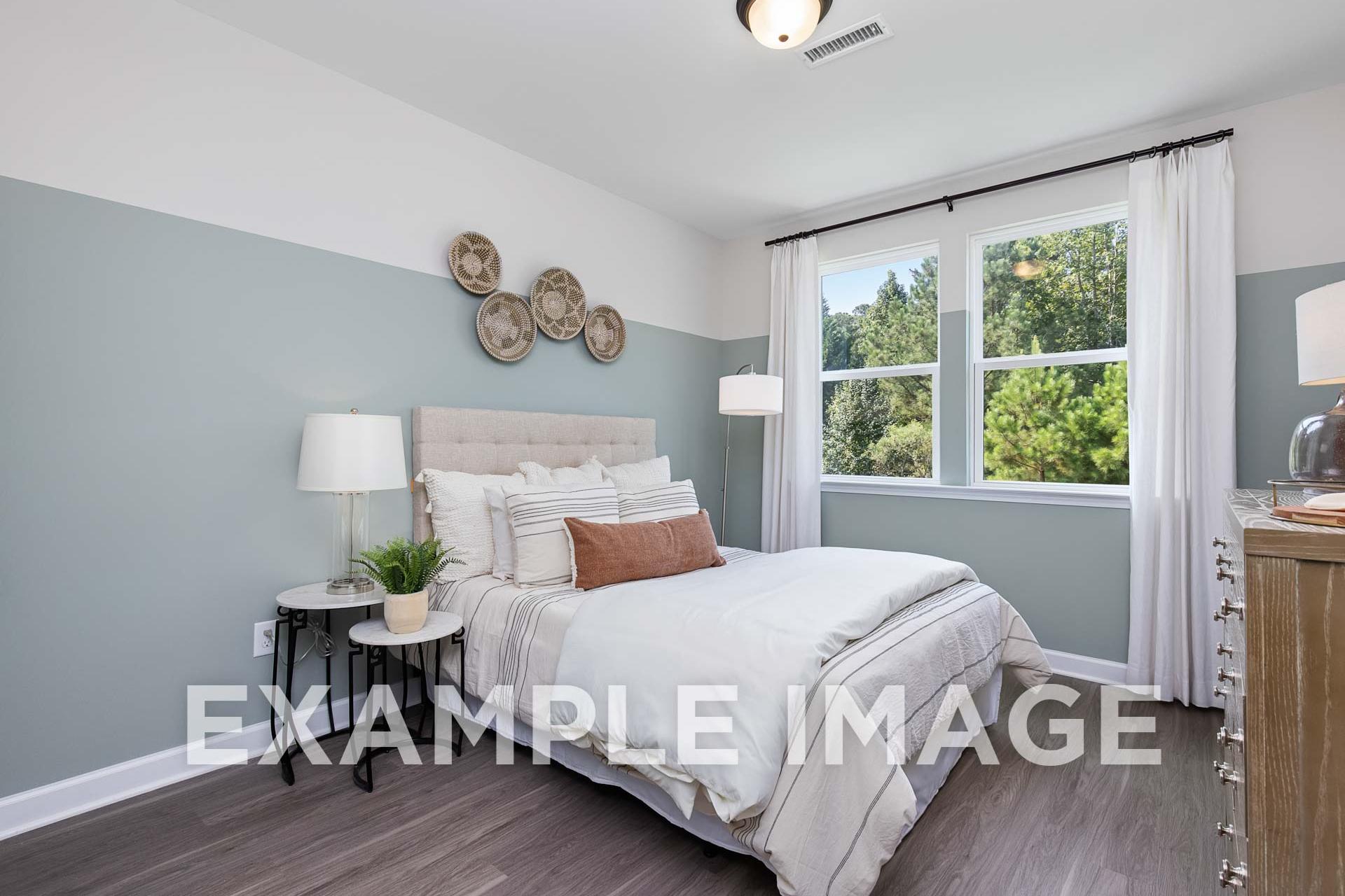 Spacious master bedroom in The Willow E with gray walls, tufted headboard bed, woven wall decor, large window, hardwood floors