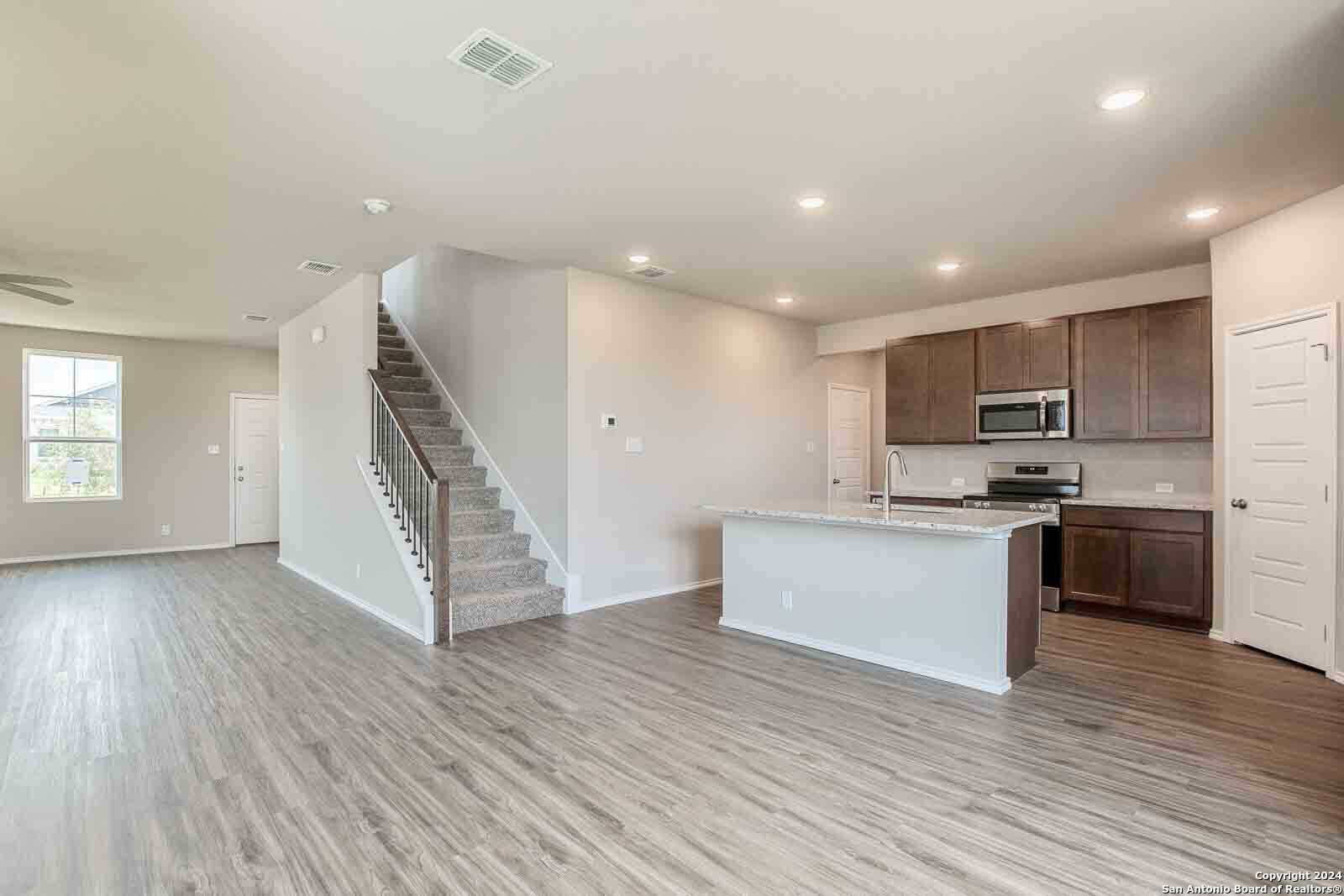 Open-concept kitchen with white island, wood cabinets, and adjacent staircase in 4-bedroom Murray H home, Hannah Heights, Seguin, Texas