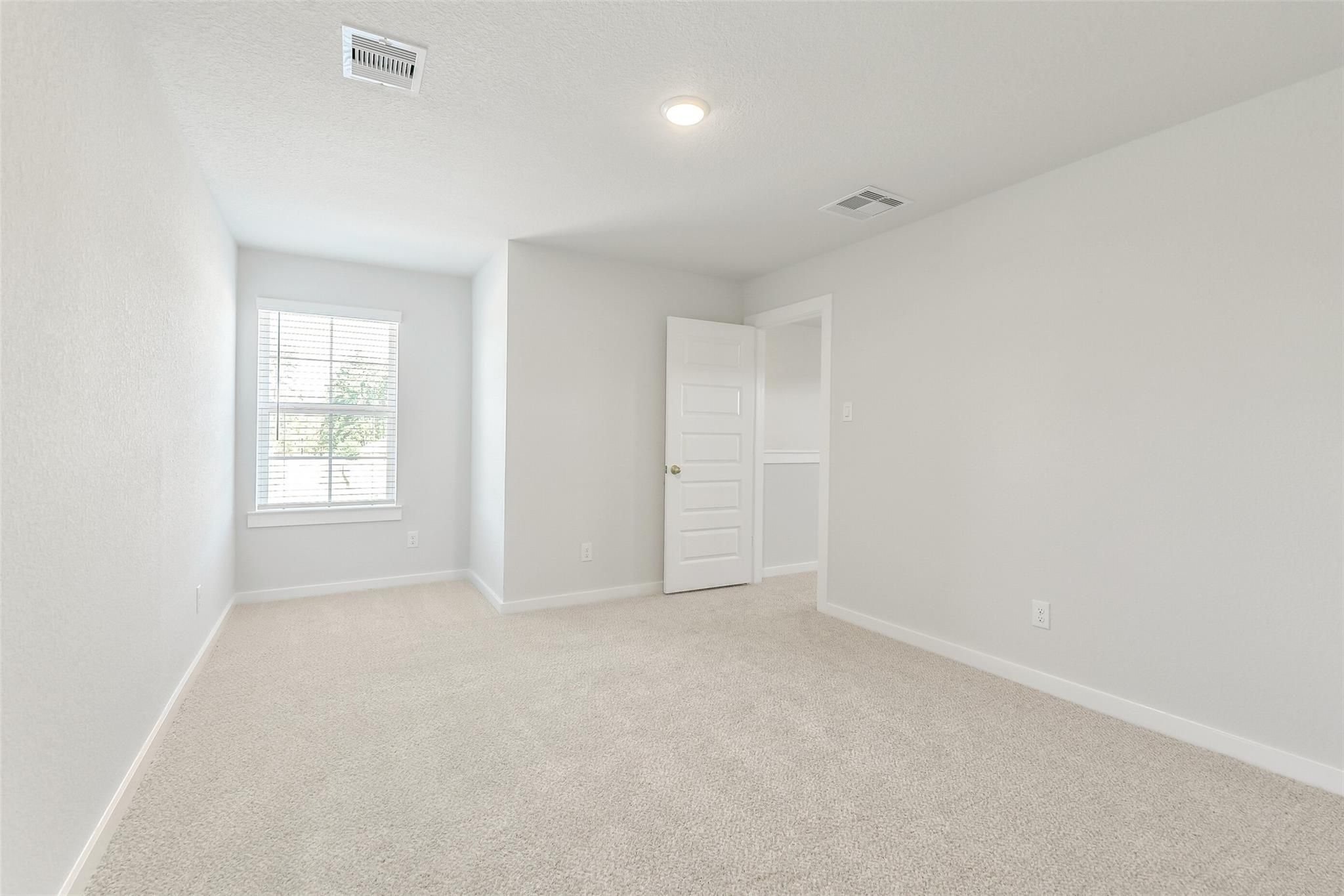 Bright secondary bedroom with large window, neutral walls, and carpeted floor in The San Marcos E home, Cleveland, Texas
